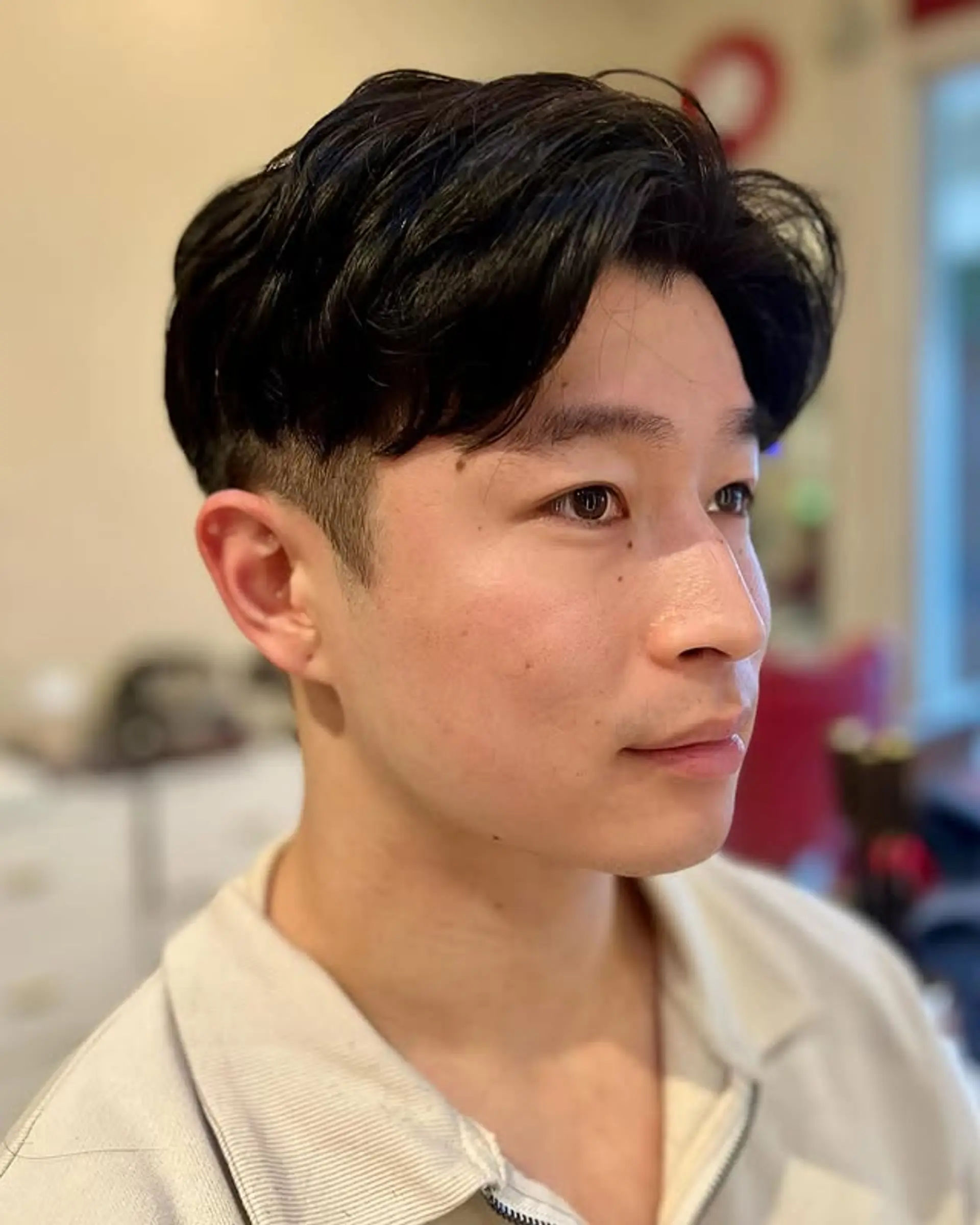 A stylish men's undercut with short, faded sides and a longer, wavy top section styled with a side-swept fringe, offering a modern and textured look. 1