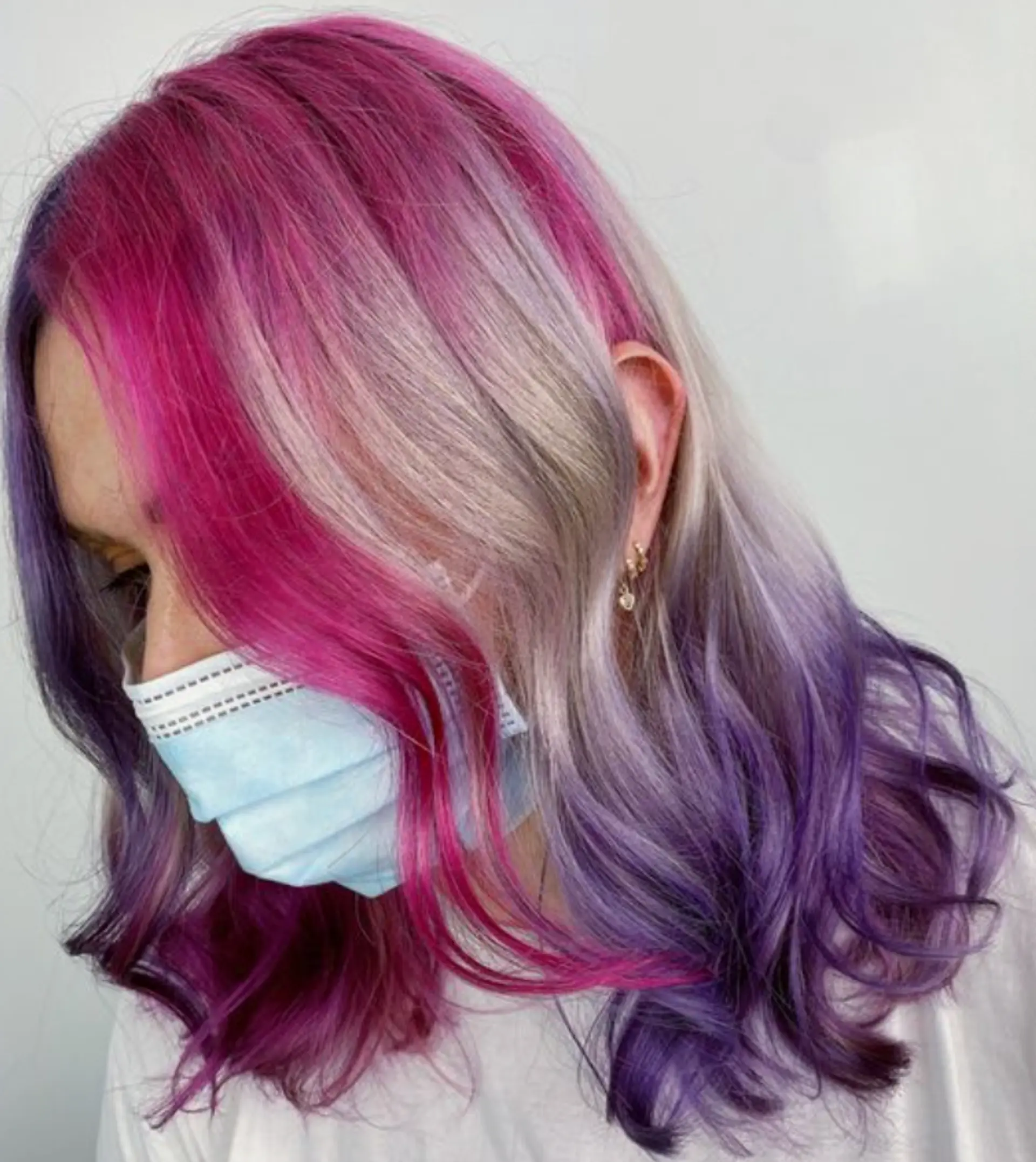 This wavy, medium-length hairstyle features a stunning rainbow cascade of pink, blonde, and purple hues. The vibrant waves create a playful, dynamic look. The layers add volume and movement to the hair, making it appear effortlessly stylish. 1