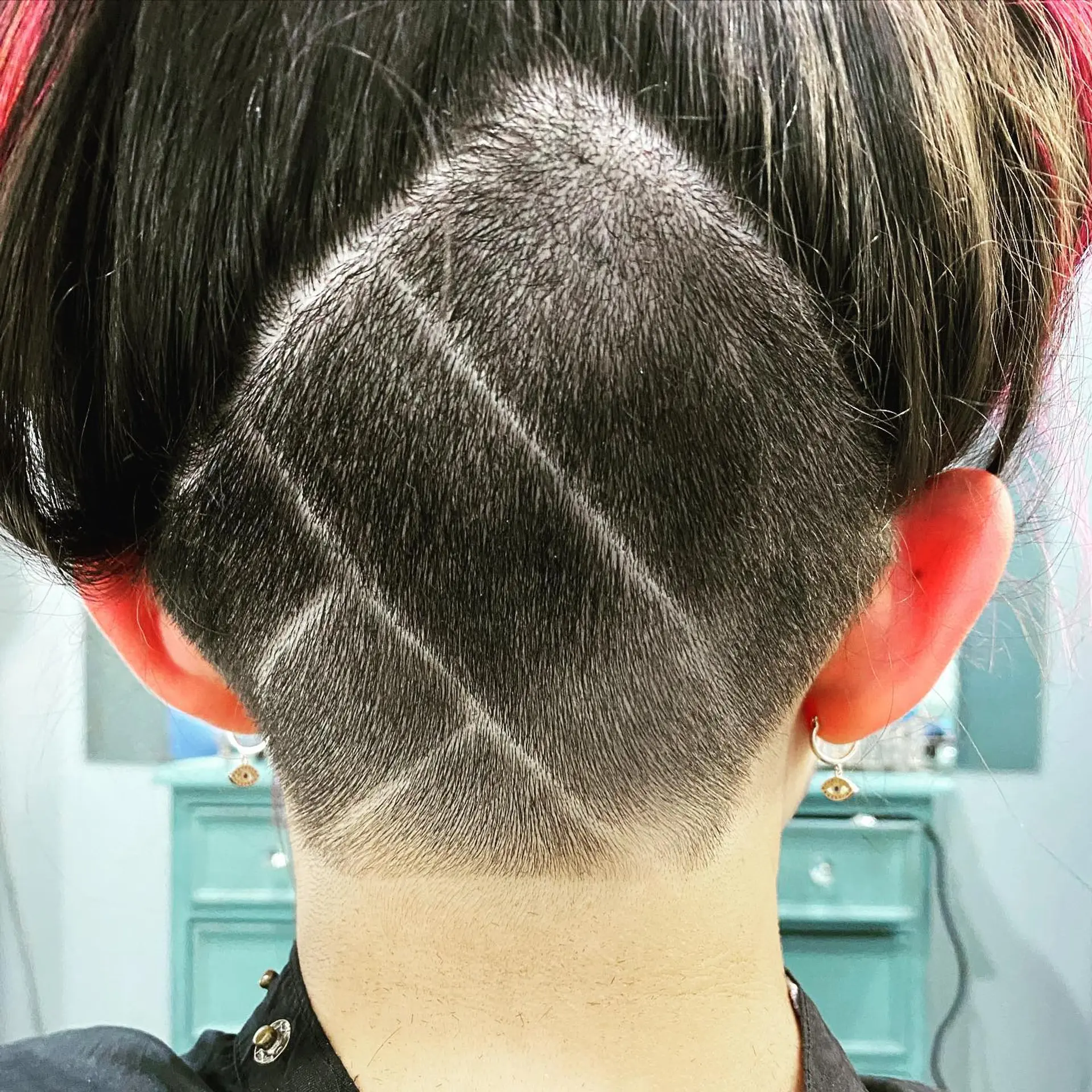 A sharp, buzzed nape undercut featuring precision shaved diagonal lines forming a geometric lattice pattern beneath dark hair. 1