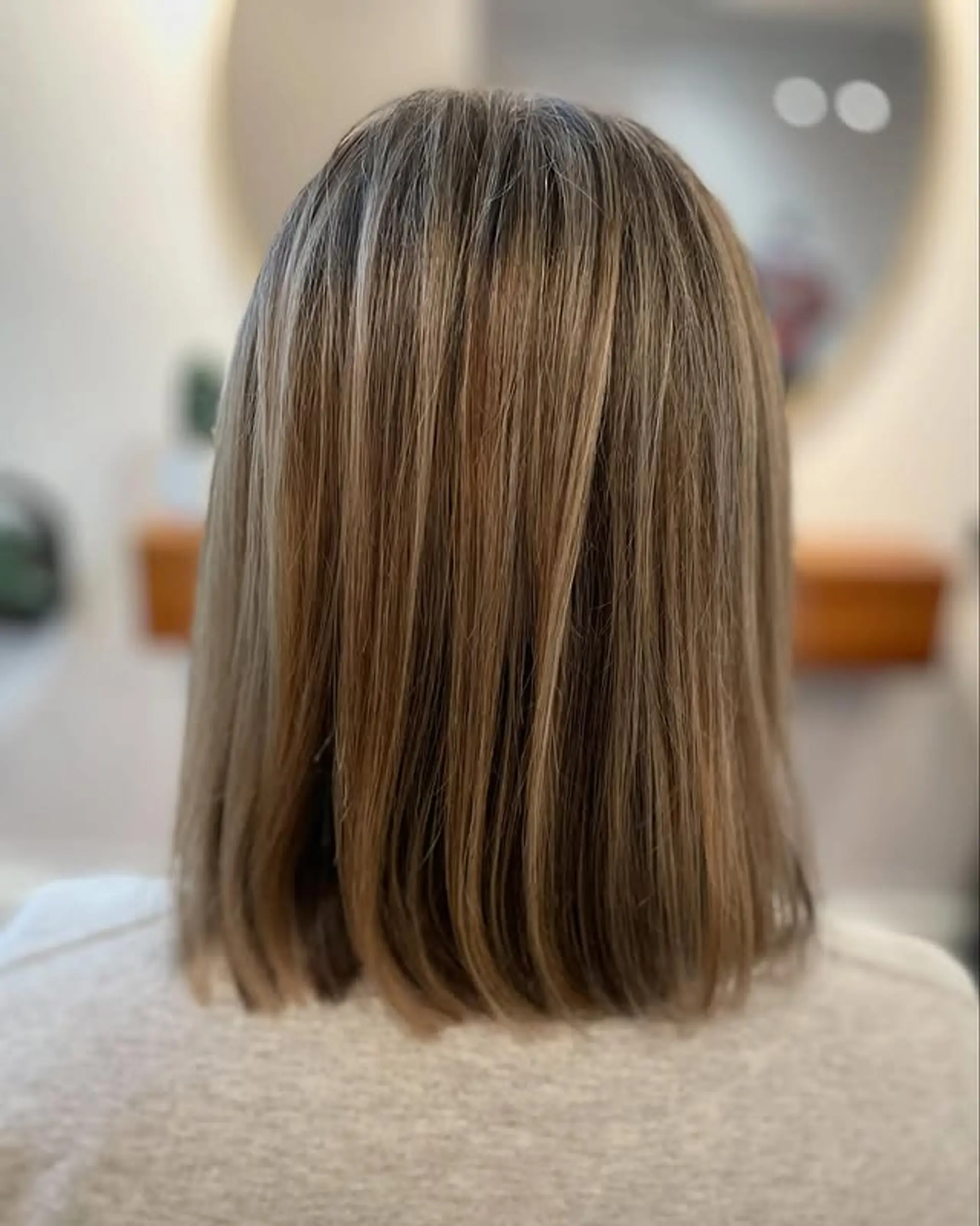 A sleek, medium-length blunt lob cut at the collarbone, featuring straight hair with delicate caramel and blonde balayage highlights for a natural, sun-kissed effect. 1