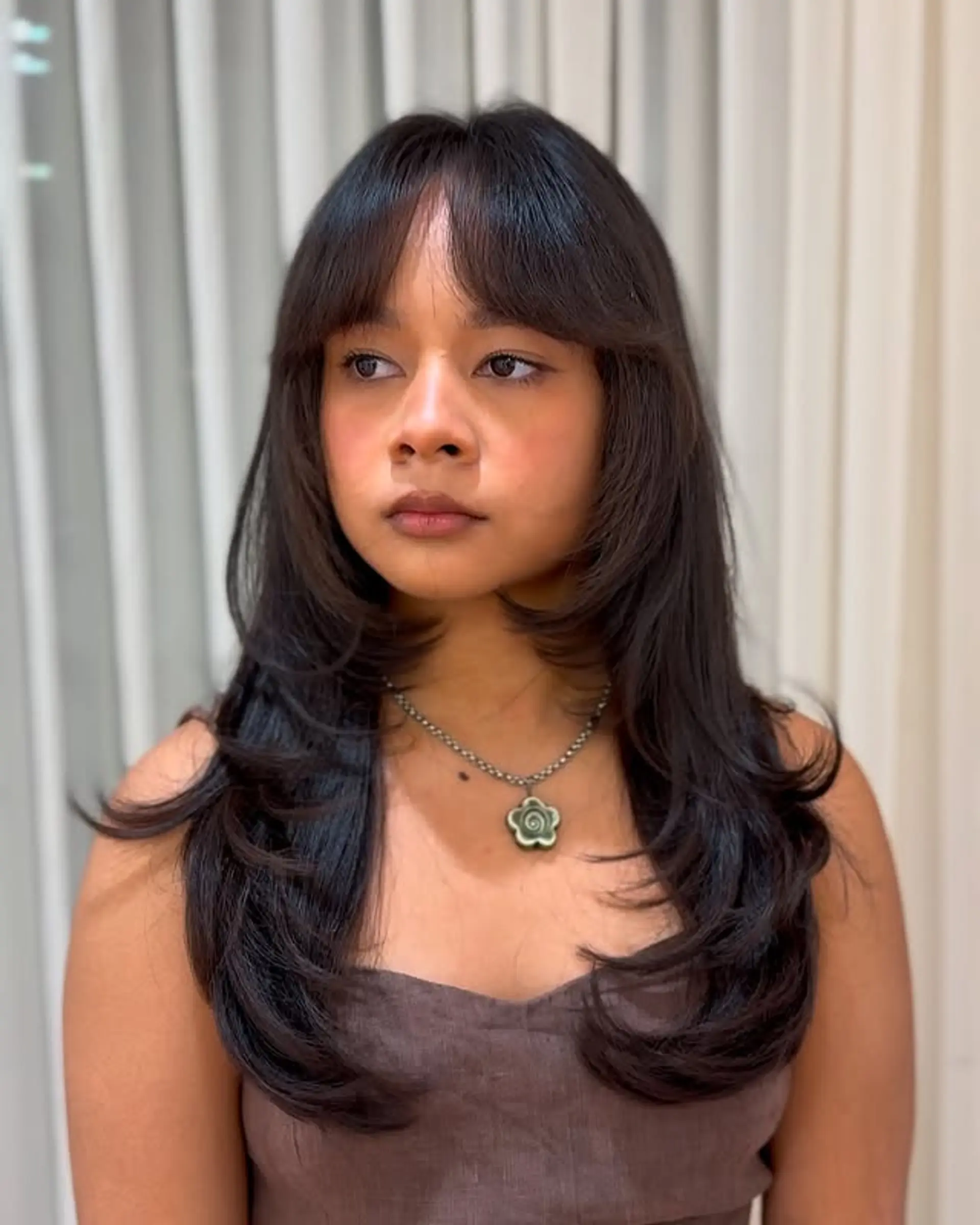 A layered medium-length hairstyle featuring face-framing layers and trendy curtain bangs. 1