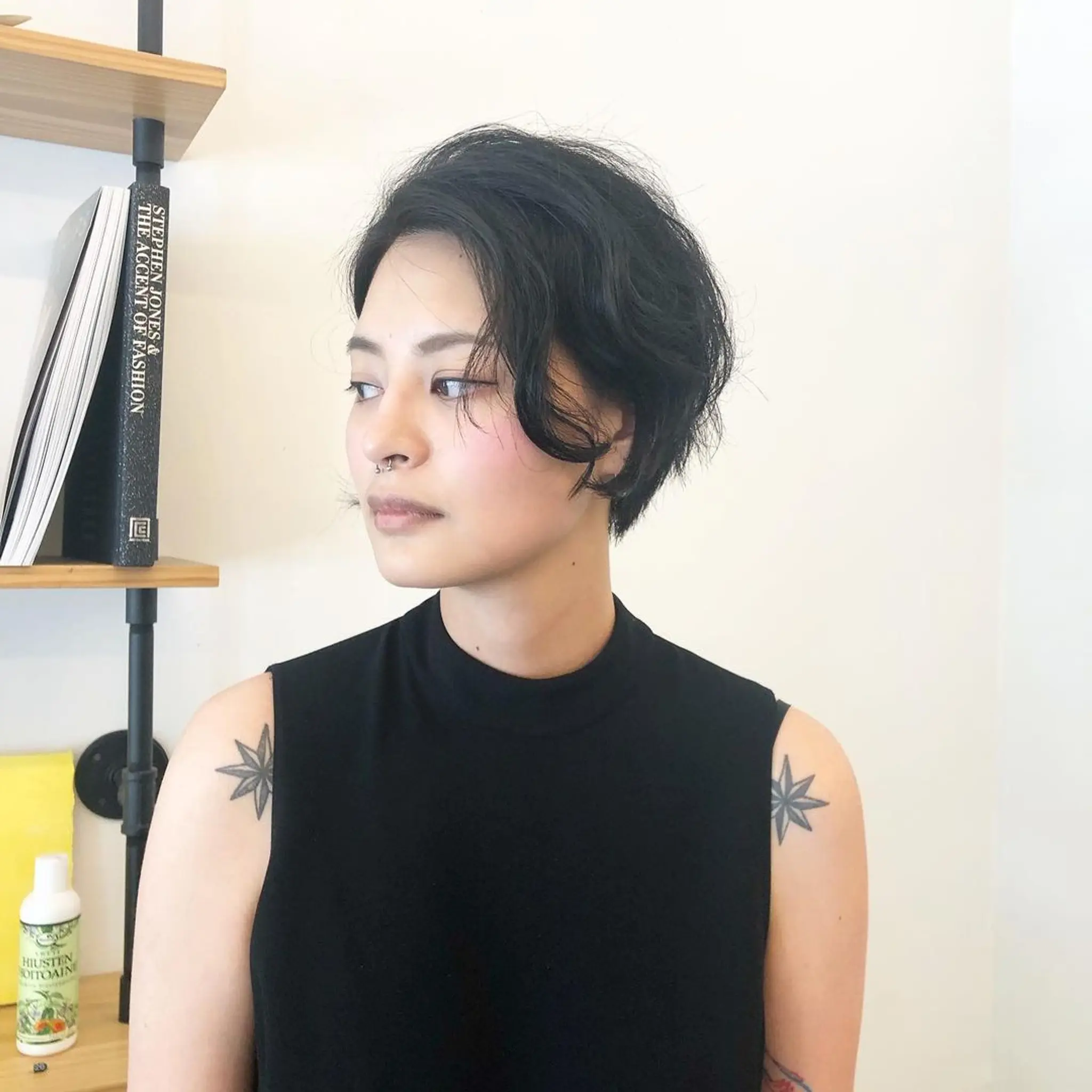 A short, black, wavy cut with asymmetrical design, textured layers, side-swept bangs, and volume on top, offering a natural, tousled look. 