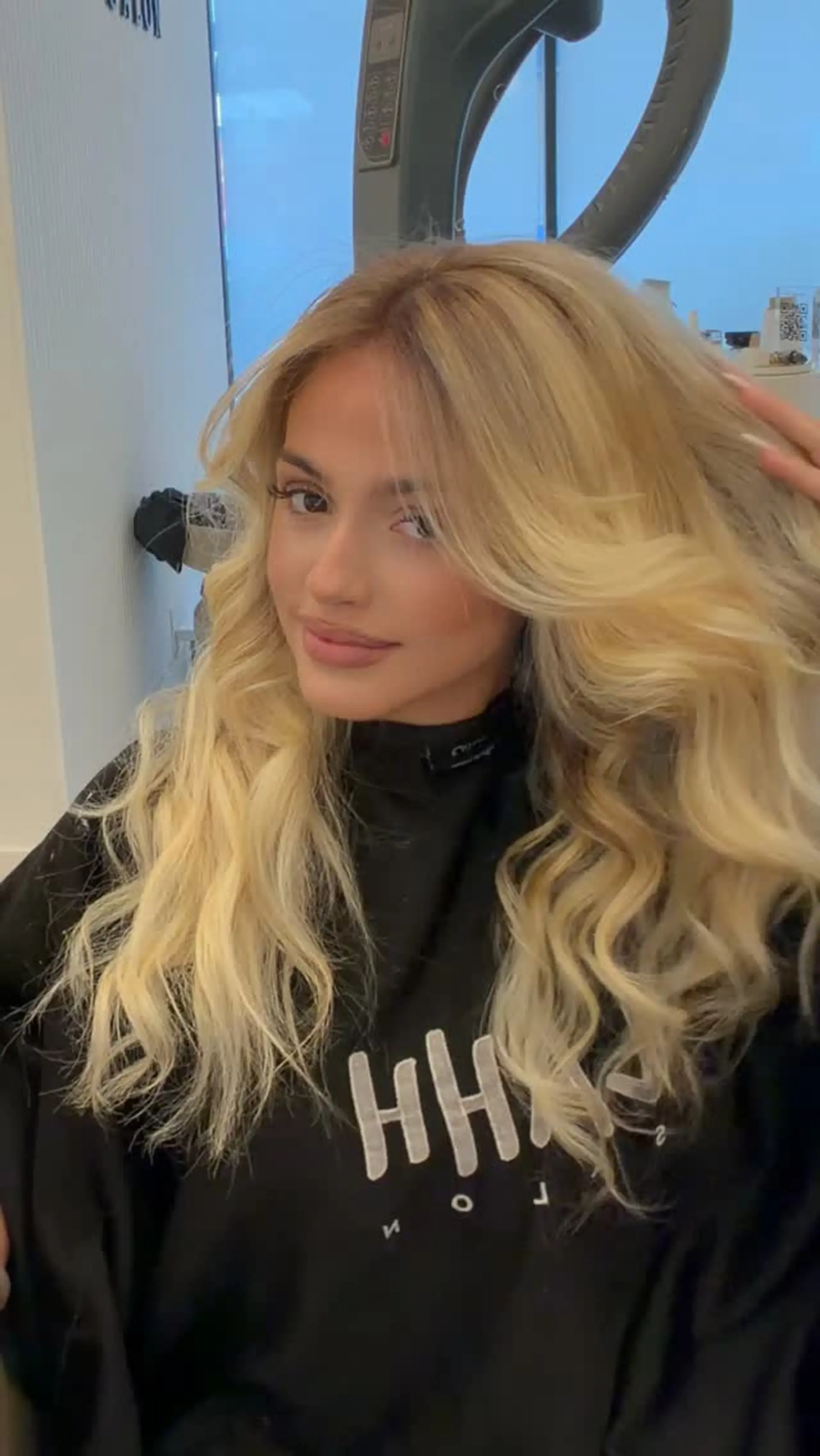 Voluminous long blonde hair styled with bouncy, face-framing blowout waves and a soft root shadow. 1