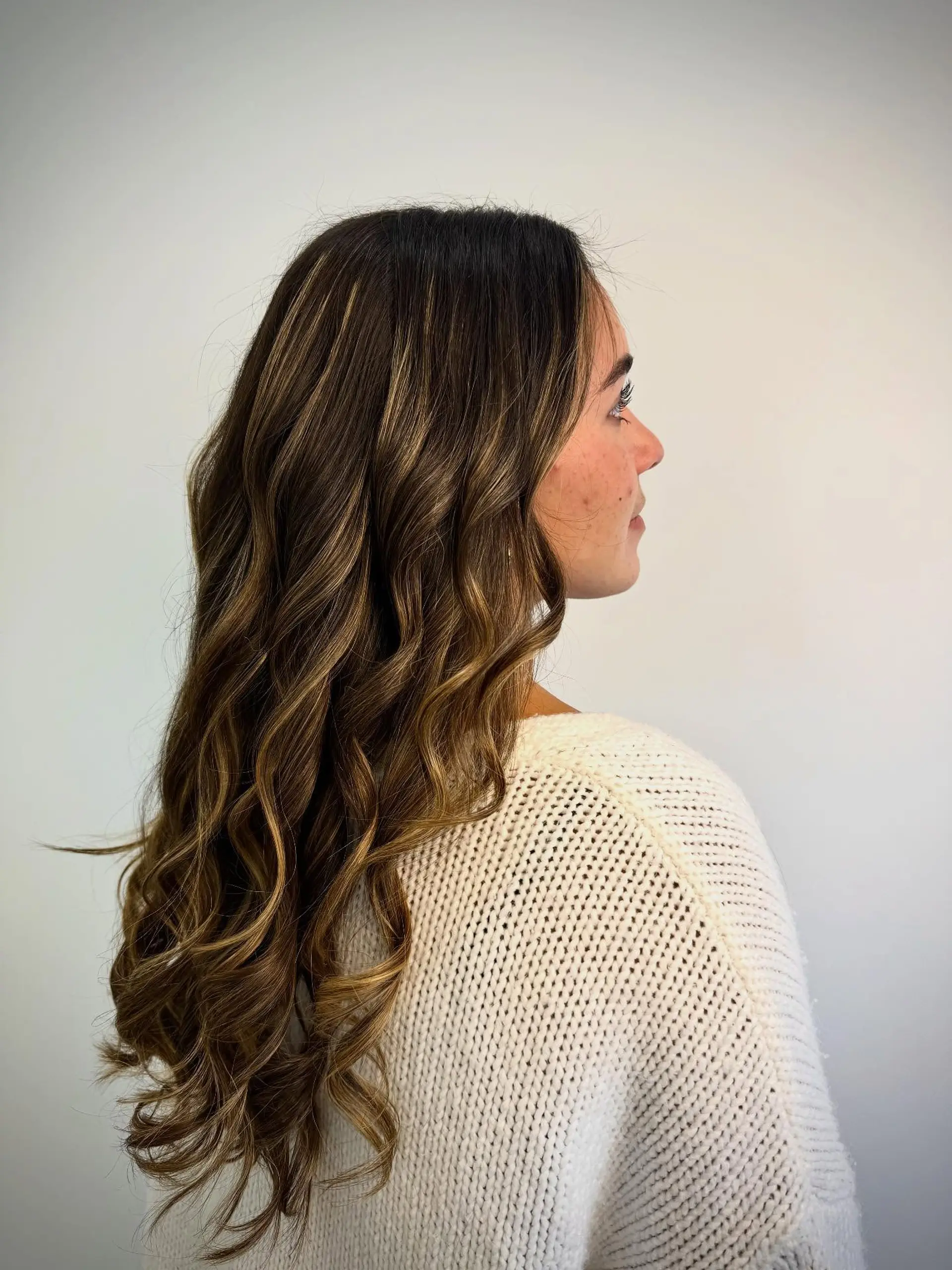 Long brown hair styled with loose, polished waves and dimensional warm caramel highlights. 1