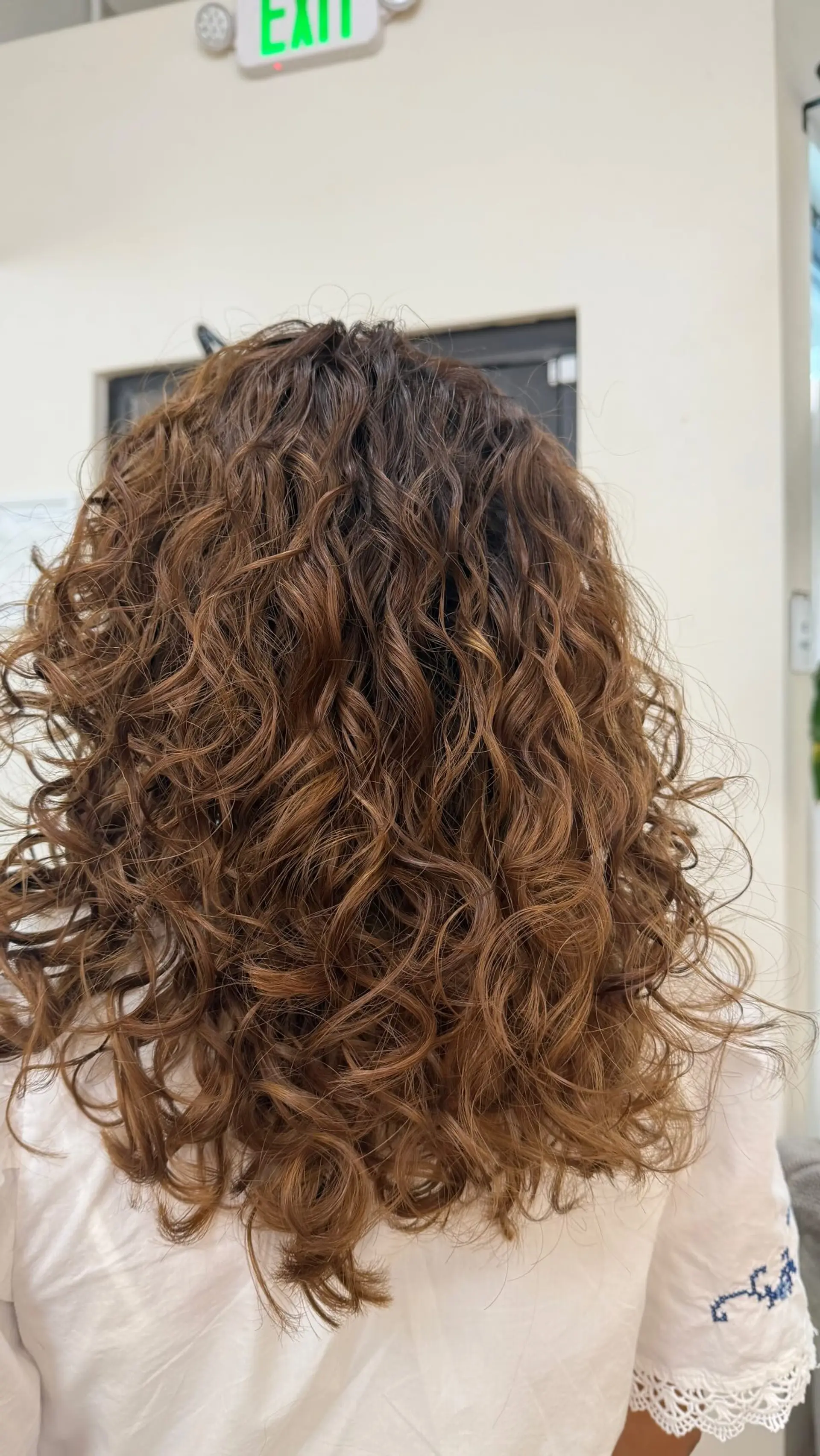 Medium-length defined curly hair cut into rounded, textured layers showcasing natural ringlets and warm dimensional tones. 1