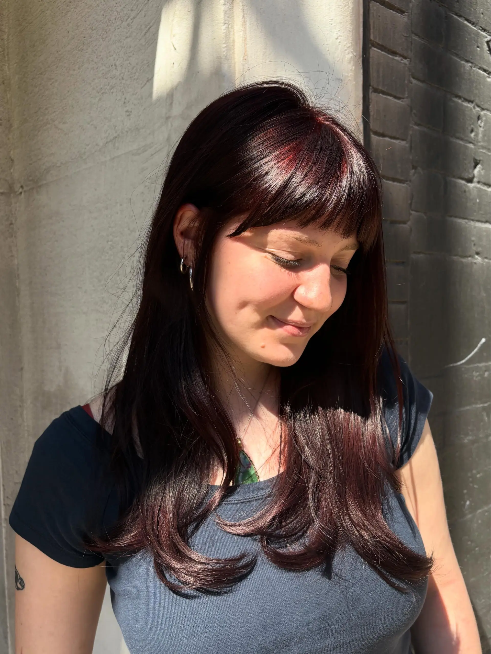 Long deep cherry brown hair styled sleek with a subtle flip at the ends and a full, eyebrow-skimming fringe. 1