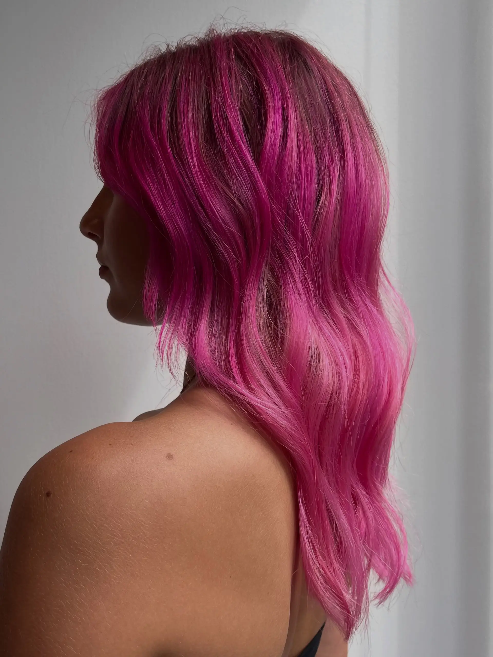 Medium-length vibrant hot pink hair cut with soft textured layers and styled into loose waves. 1