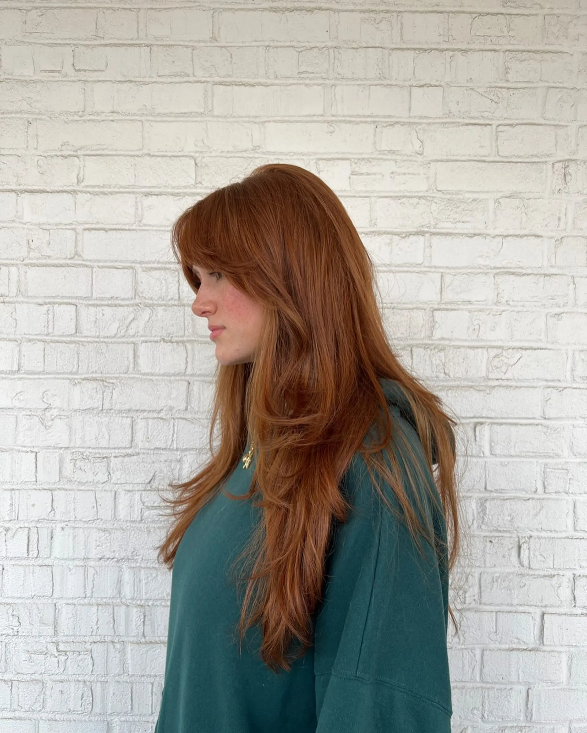 Long vibrant copper hair featuring soft face-framing curtain bangs and seamless layers with a smooth blowout finish. 1