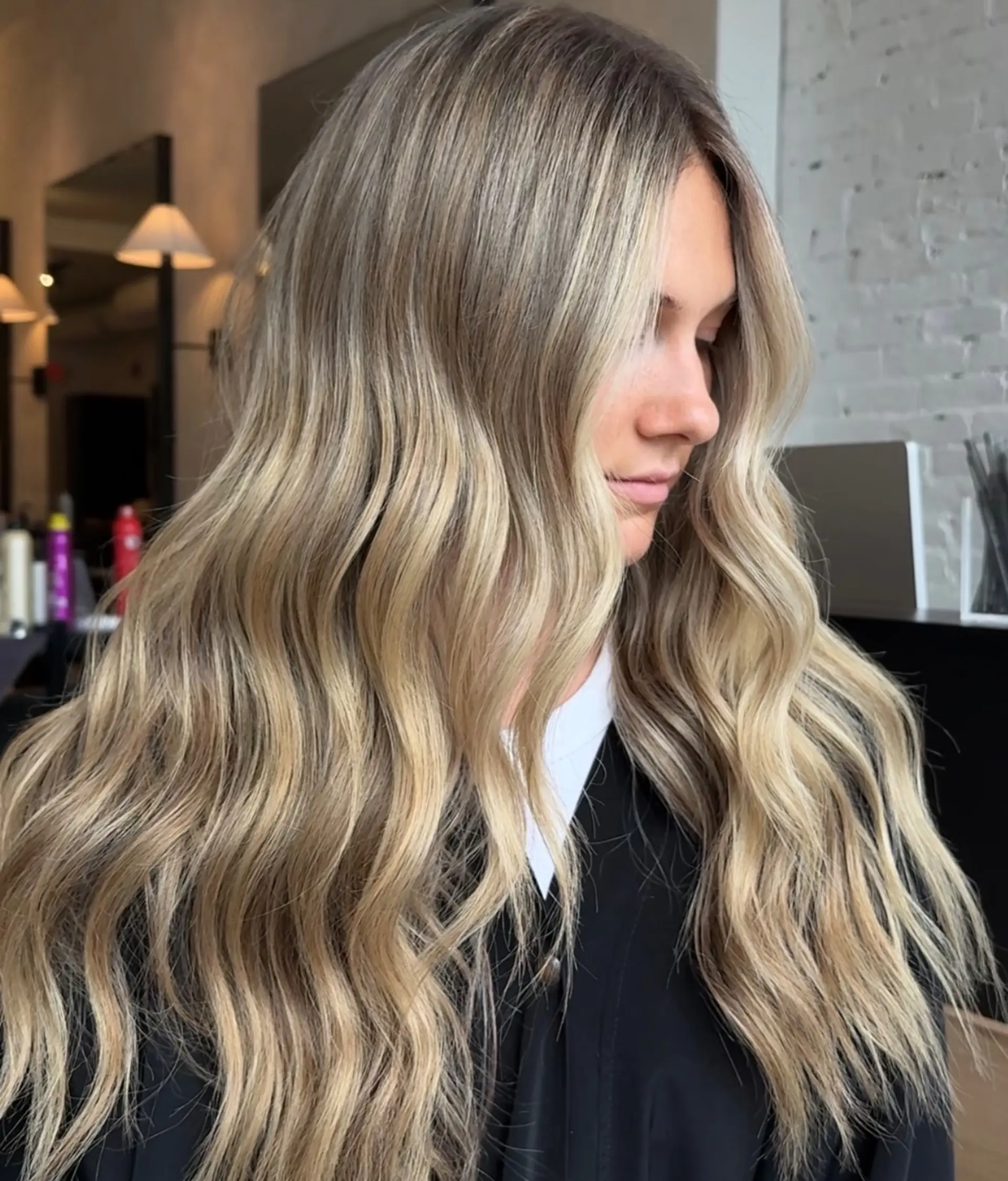 Long dimensional blonde hair styled in soft, undone beach waves with brighter face-framing strands. 1