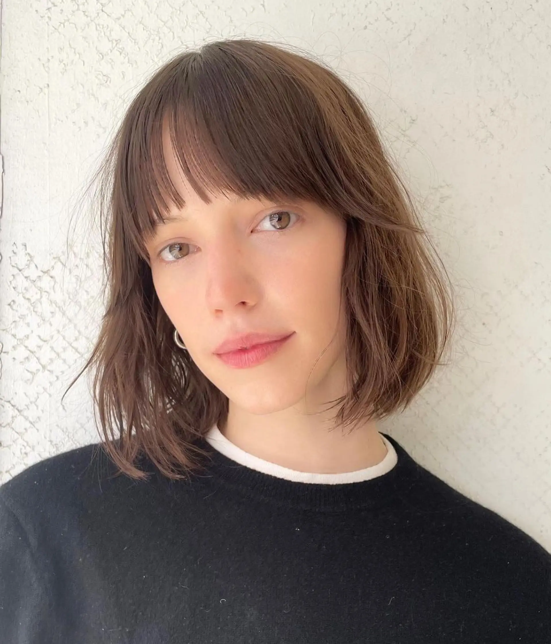A medium-length chic shaggy bob with dark brown wavy hair, featuring blunt bangs and tousled layers. 2
