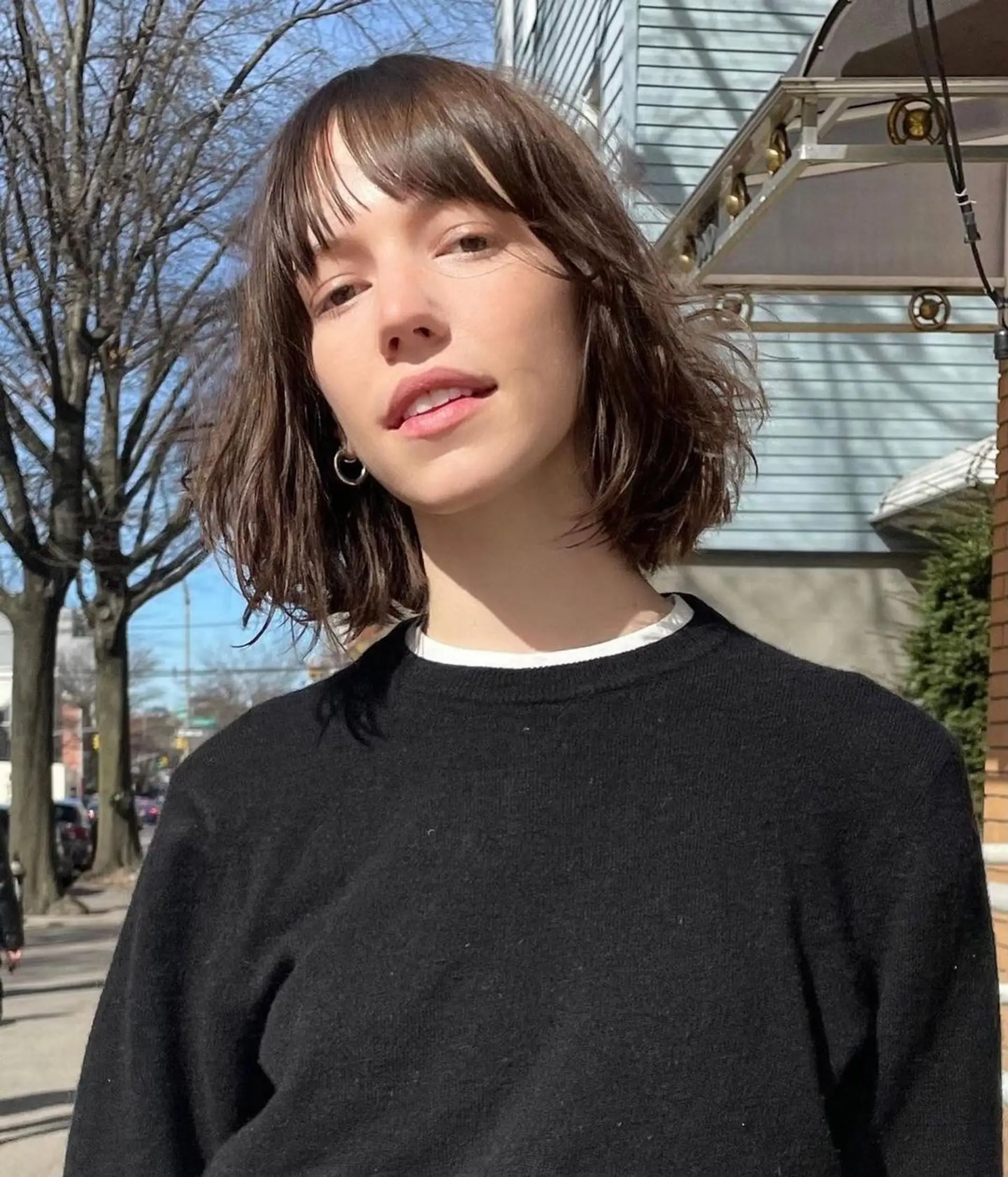 A medium-length chic shaggy bob with dark brown wavy hair, featuring blunt bangs and tousled layers. 3