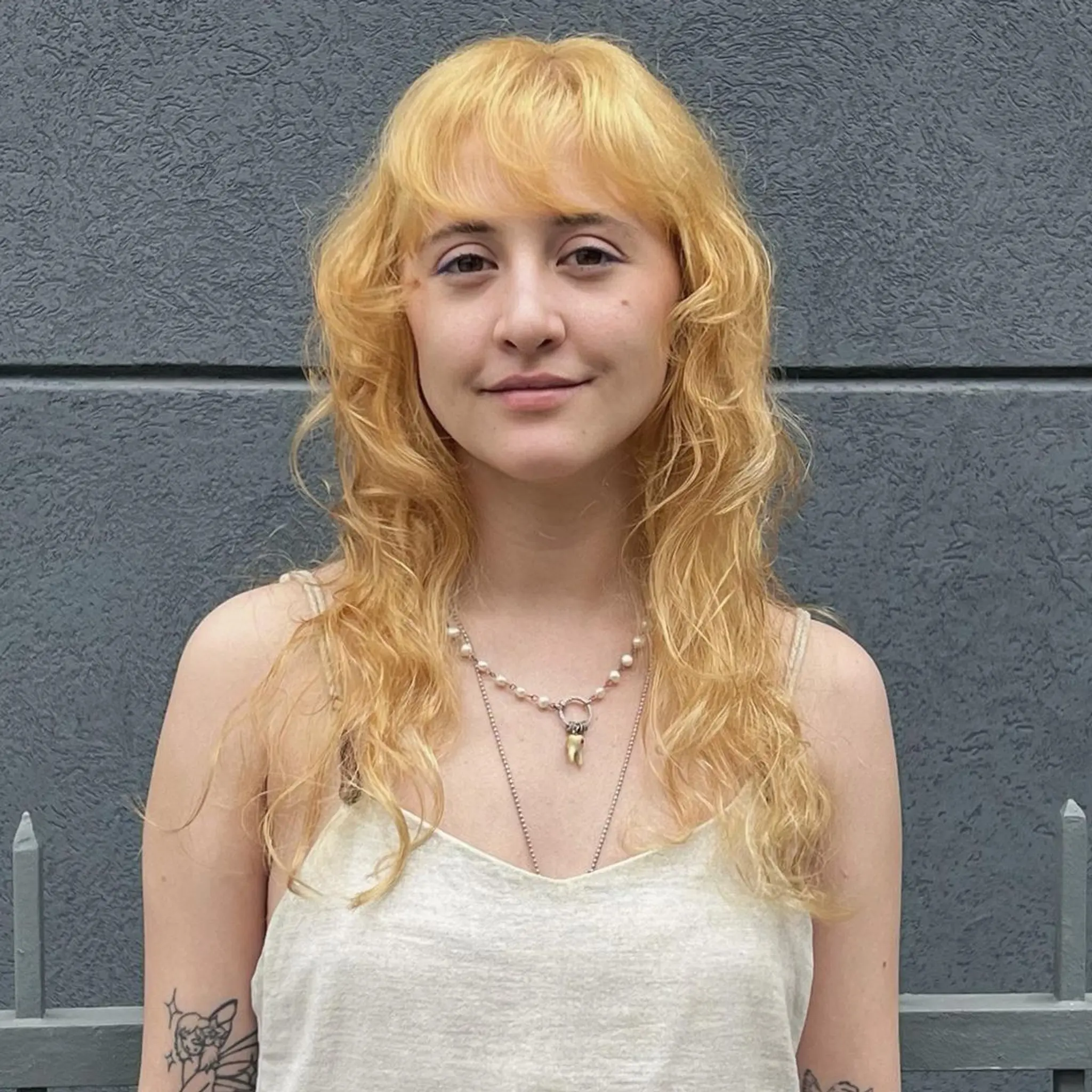 Medium-length, golden blonde hair with natural waves. Features fringe bangs and a layered cut, giving a sunlit, radiant look.
