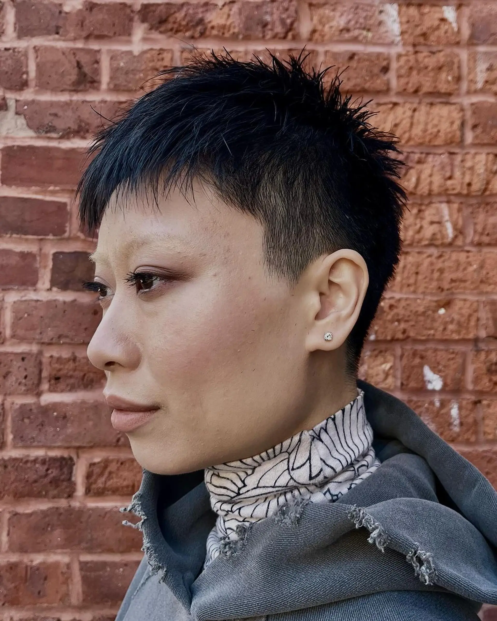 An edgy modern short pixie cut with a unique undercut, textured spiky top, and a short irregular fringe, all in black. 1