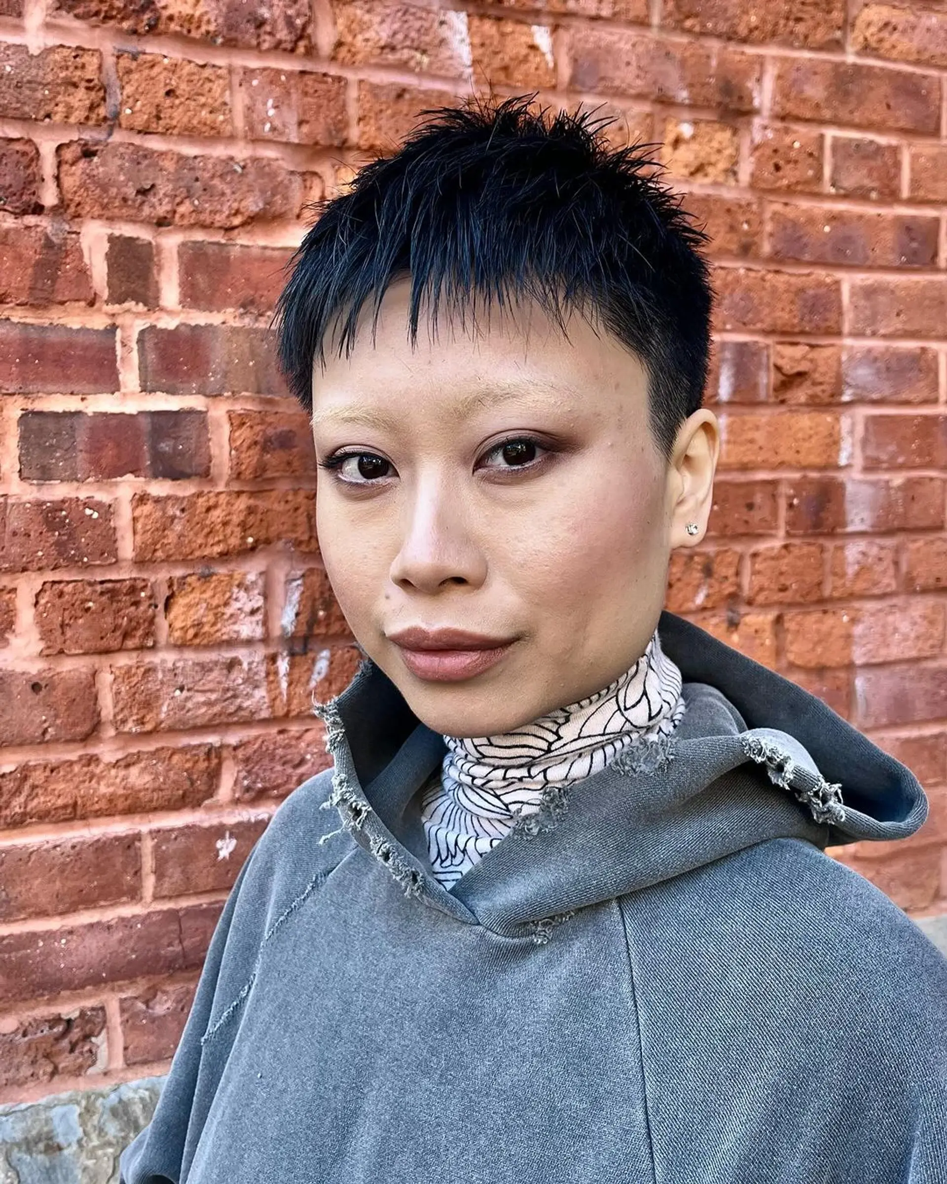 An edgy modern short pixie cut with a unique undercut, textured spiky top, and a short irregular fringe, all in black. 2