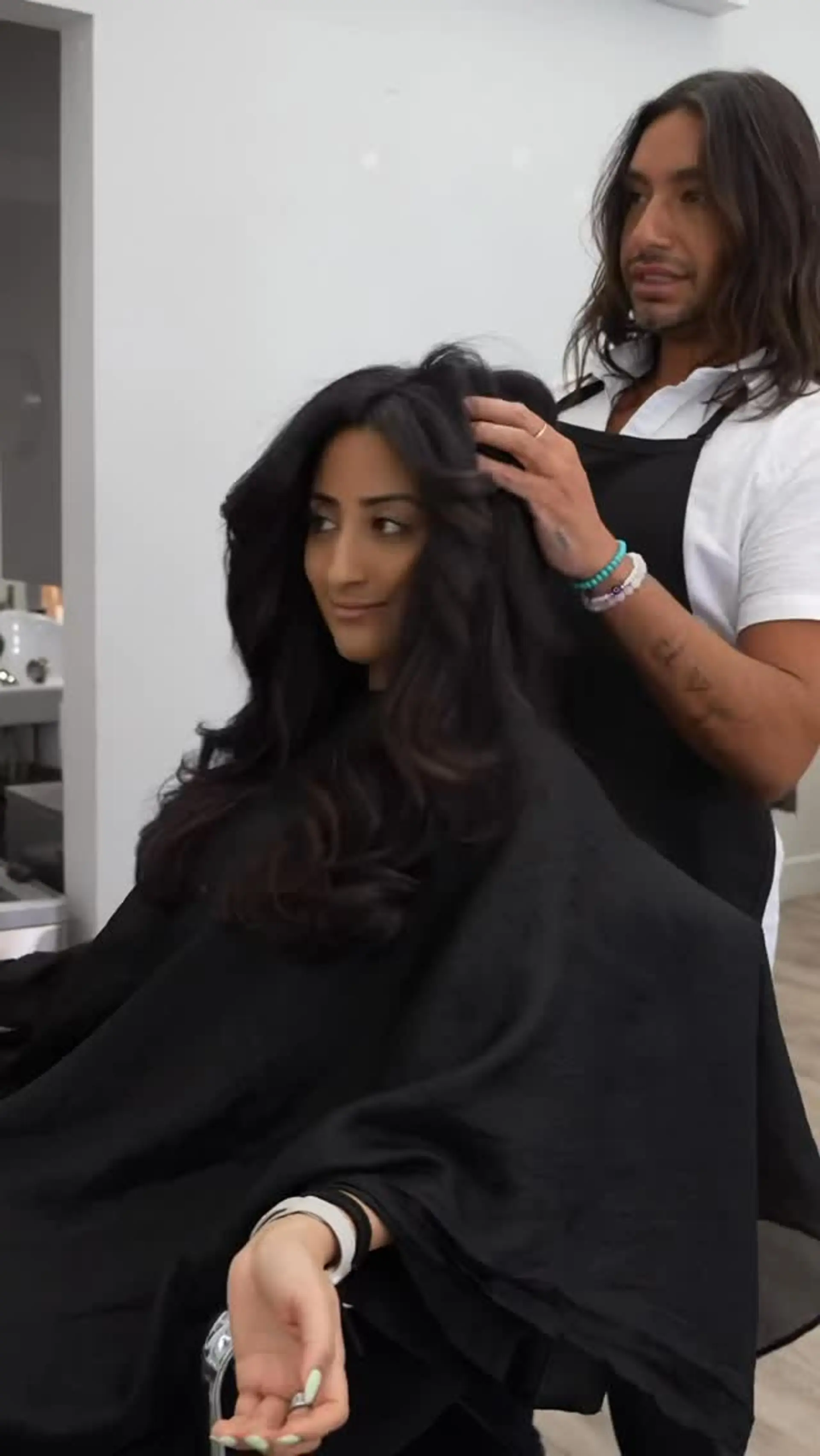 Voluminous, long dark hair styled with soft bouncy waves and face-framing layers. 1