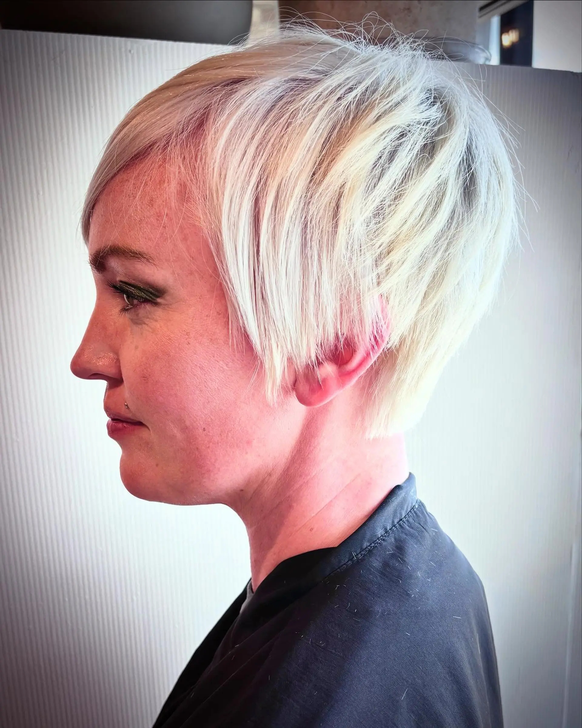 A modern platinum blonde pixie cut with fine, wispy layering and side-swept bangs. 1
