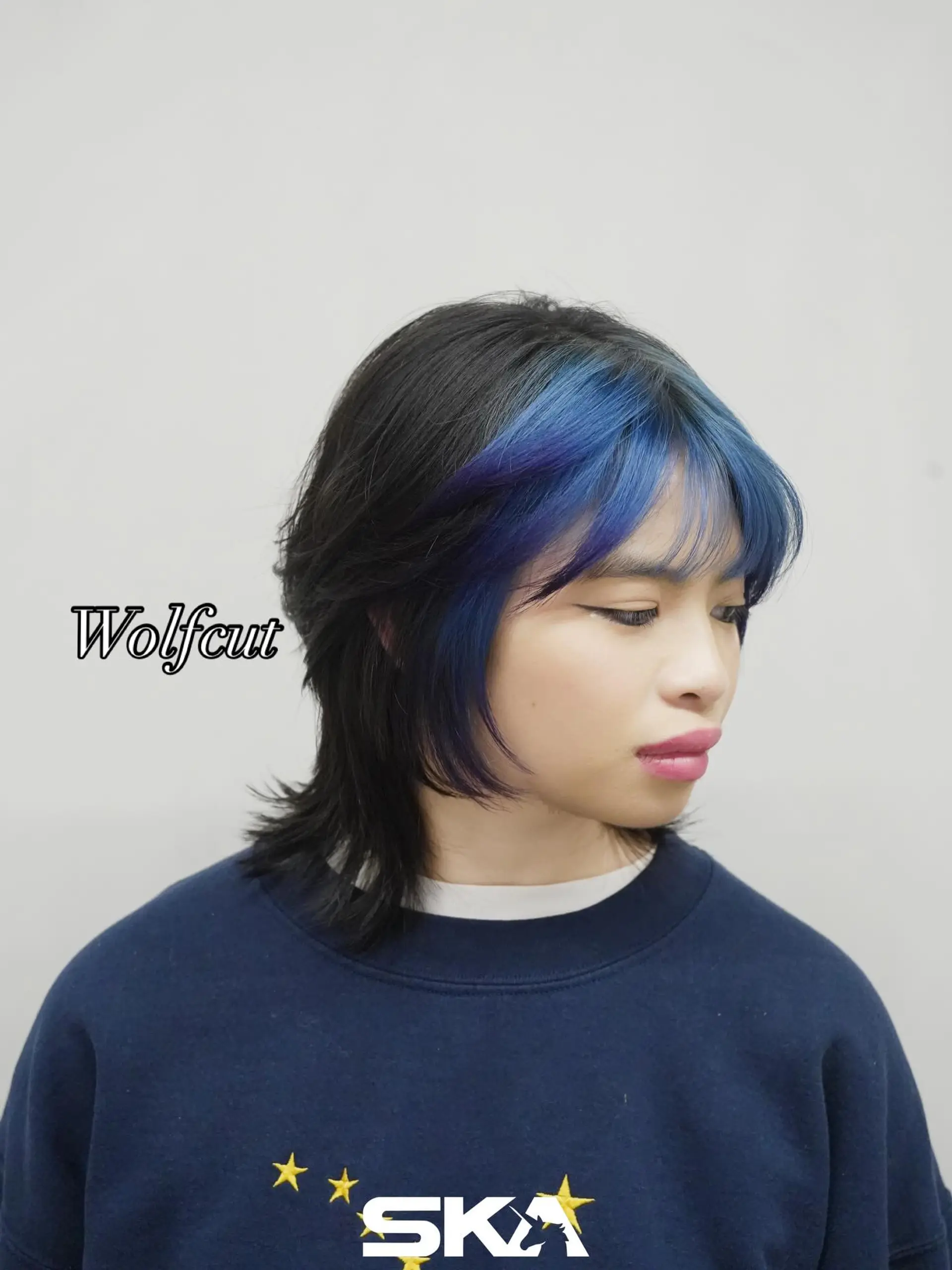 A textured wolf cut featuring black hair with vibrant cobalt blue and violet face-framing bangs. 1