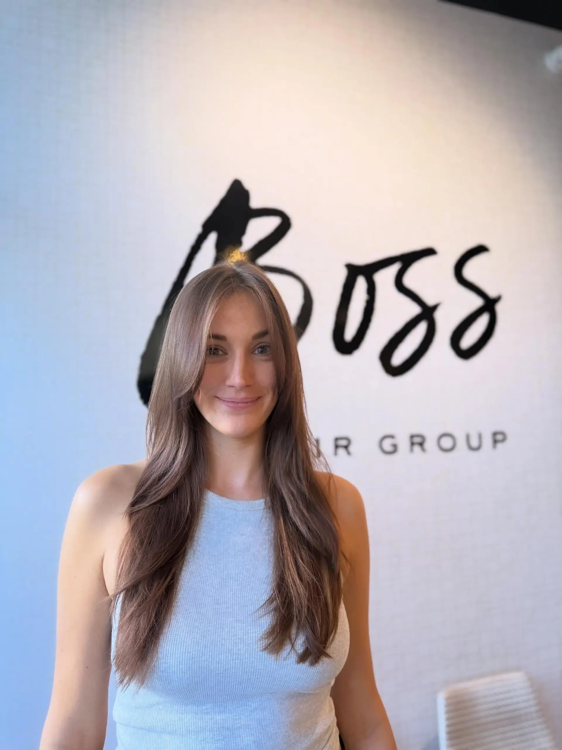 Long brunette hair cut with soft cascading layers and face-framing curtain bangs, styled in a sleek, smooth blowout. 1