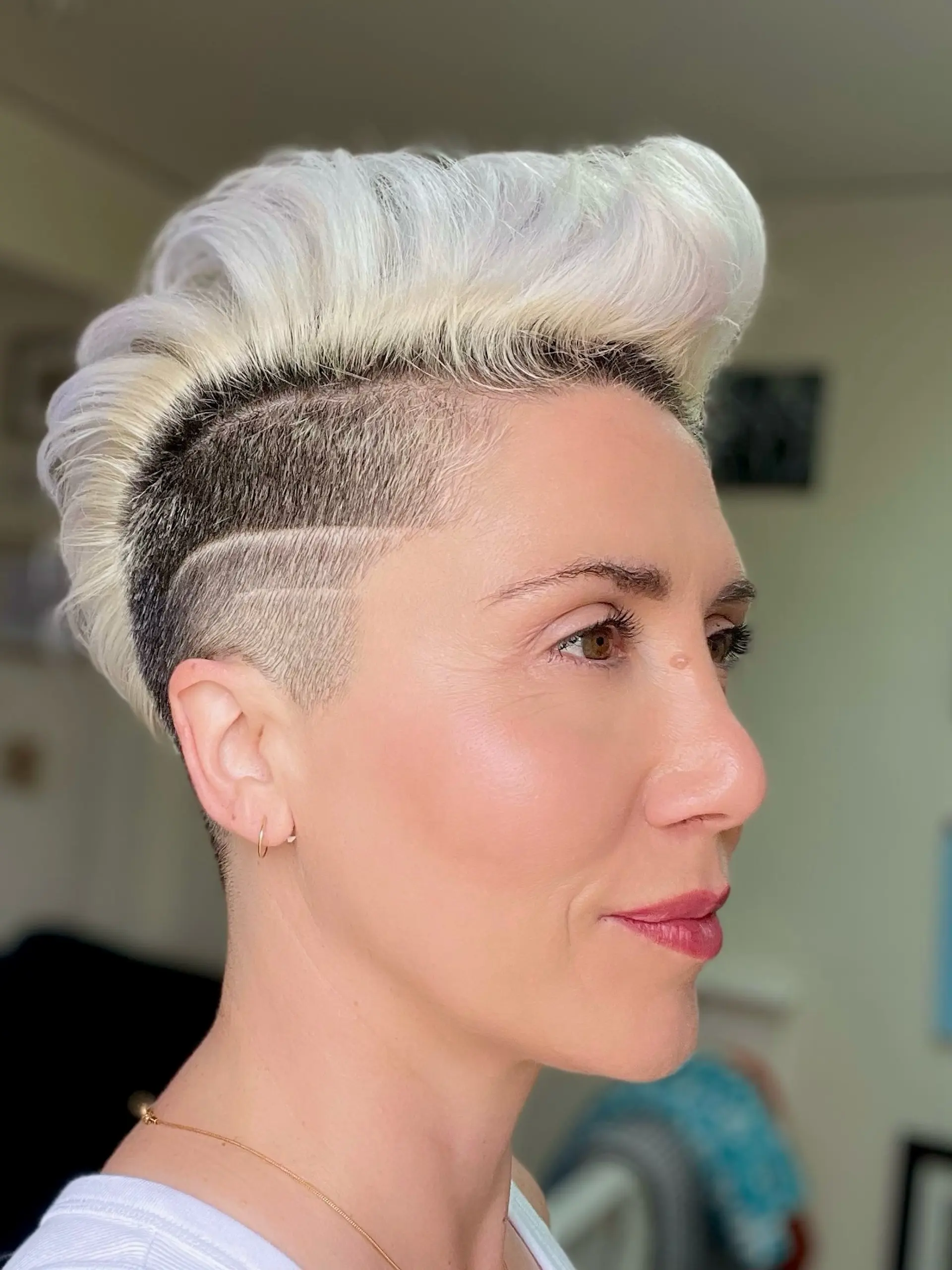 A bold short hairstyle featuring a close-cropped undercut with shaved geometric lines and a high-volume, swept-back platinum blonde top. 1