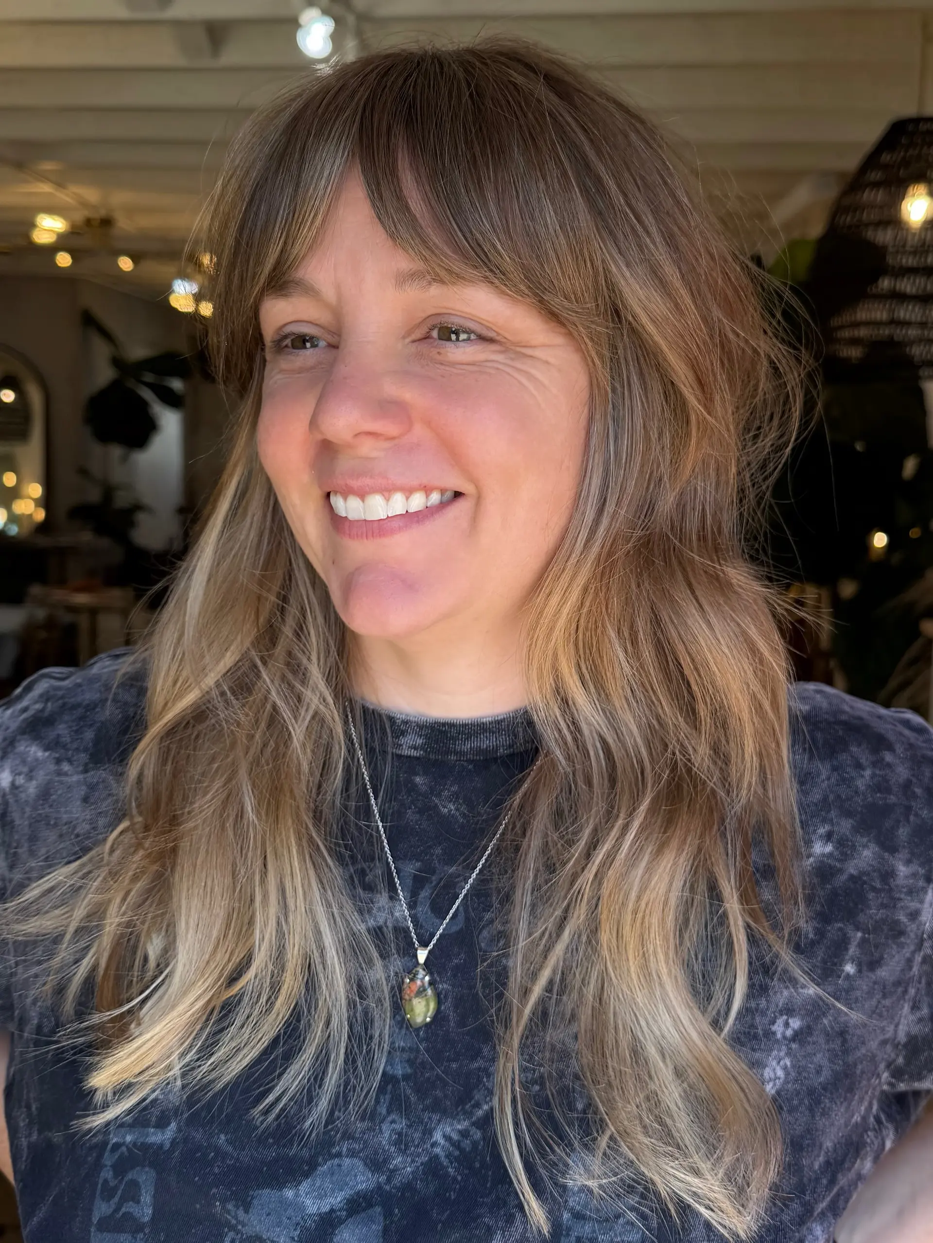 Long layered blonde hair styled with soft lived-in waves and full fringe bangs. 1