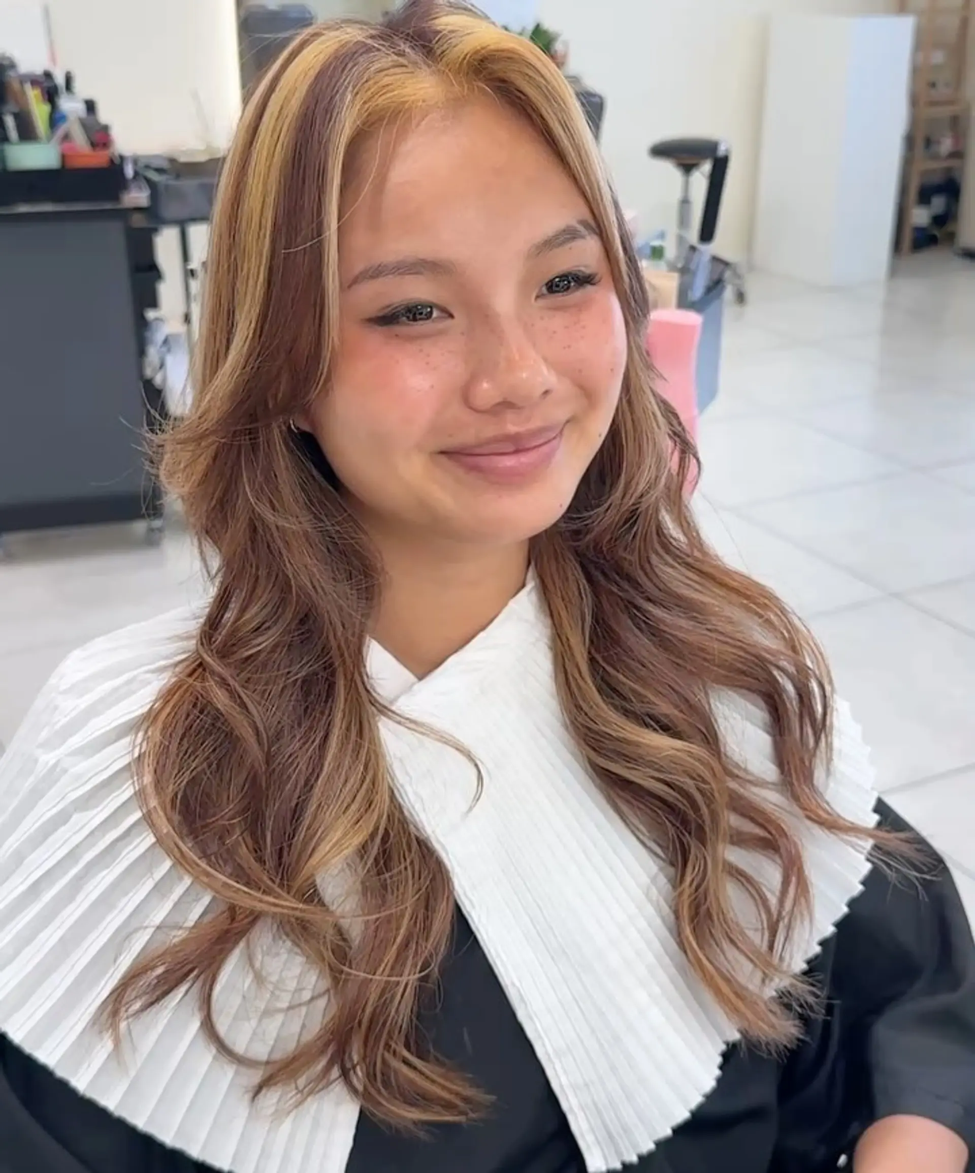 Long warm brown hair styled in soft, loose waves featuring prominent golden blonde face-framing money piece highlights. 1