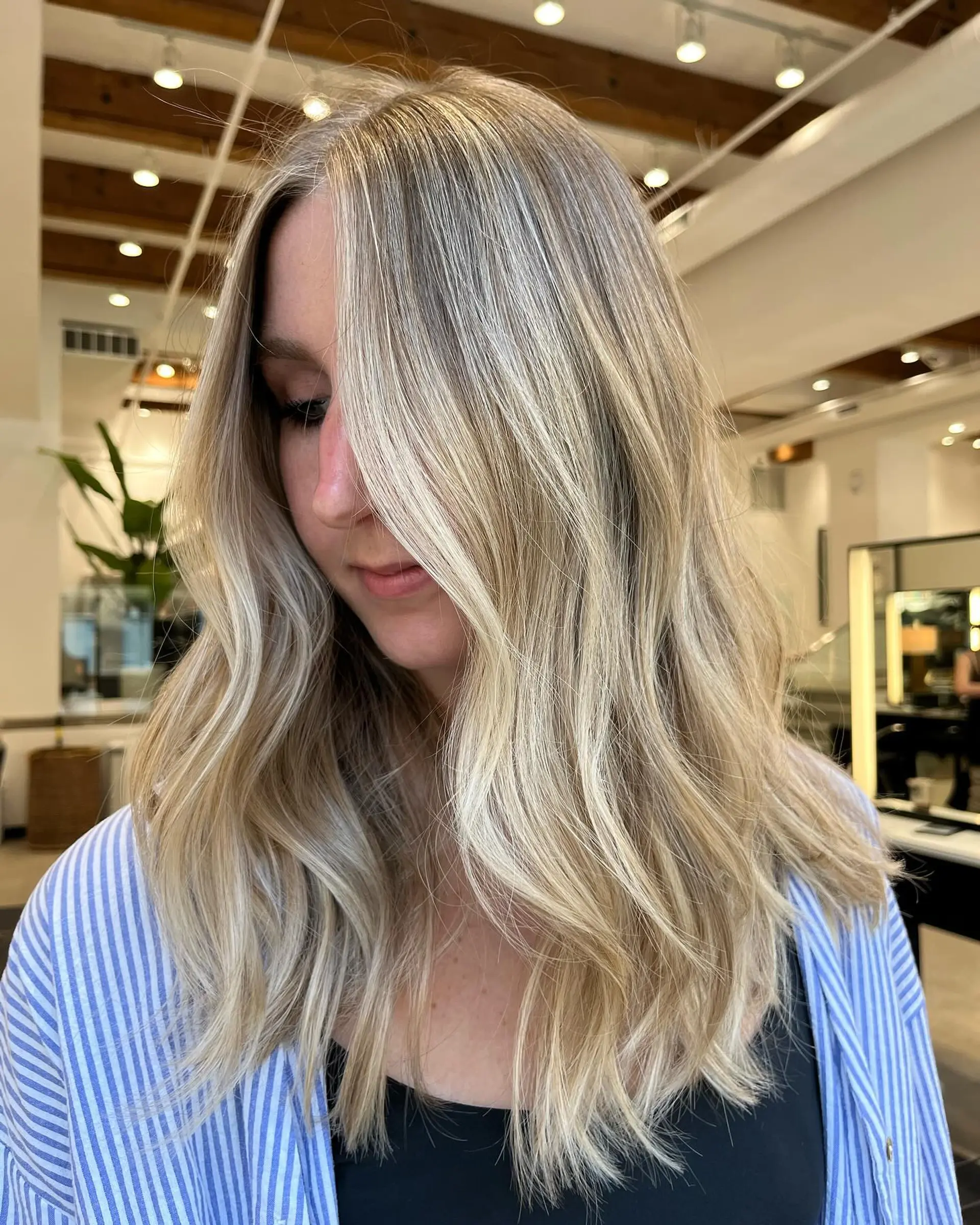 Medium length wavy hairstyle with blonde balayage and a shadow root. 1