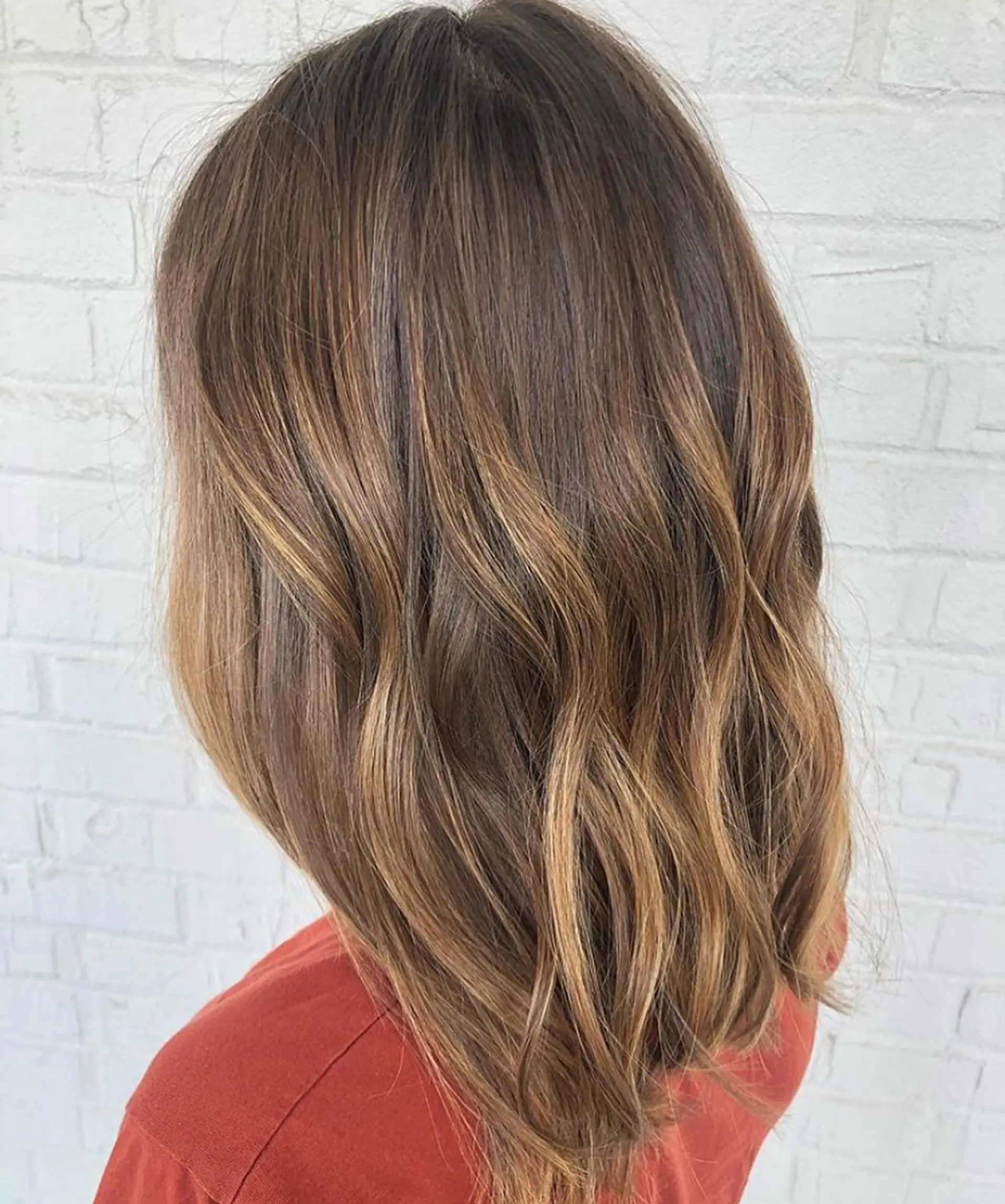 Medium-length brunette hair styled with soft, loose waves and hand-painted warm caramel balayage highlights. 1