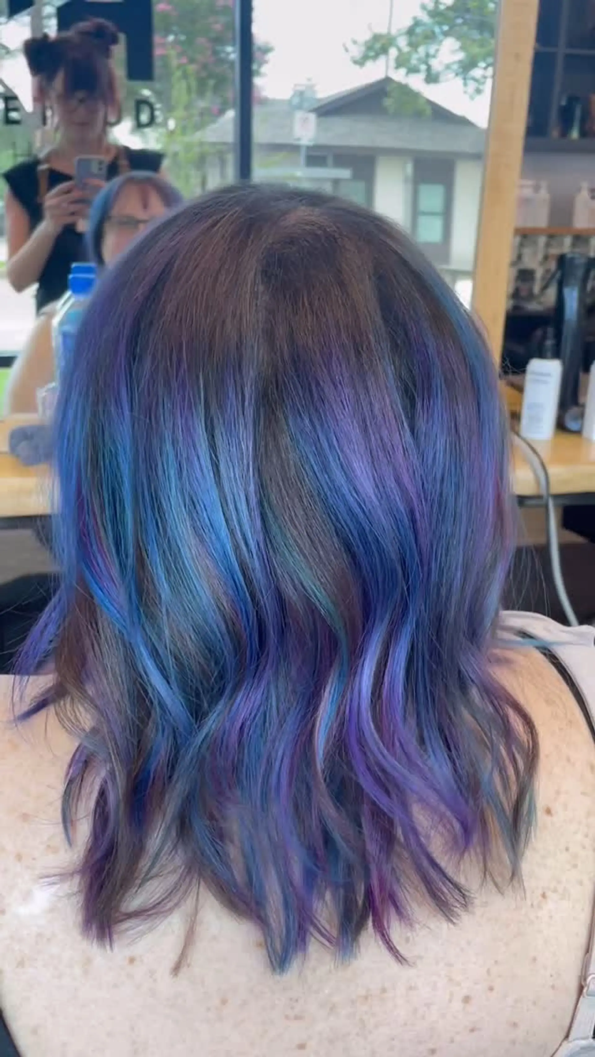 A shoulder-length wavy look featuring vibrant oil slick tones of blue and purple blended into a dark brown base. 1