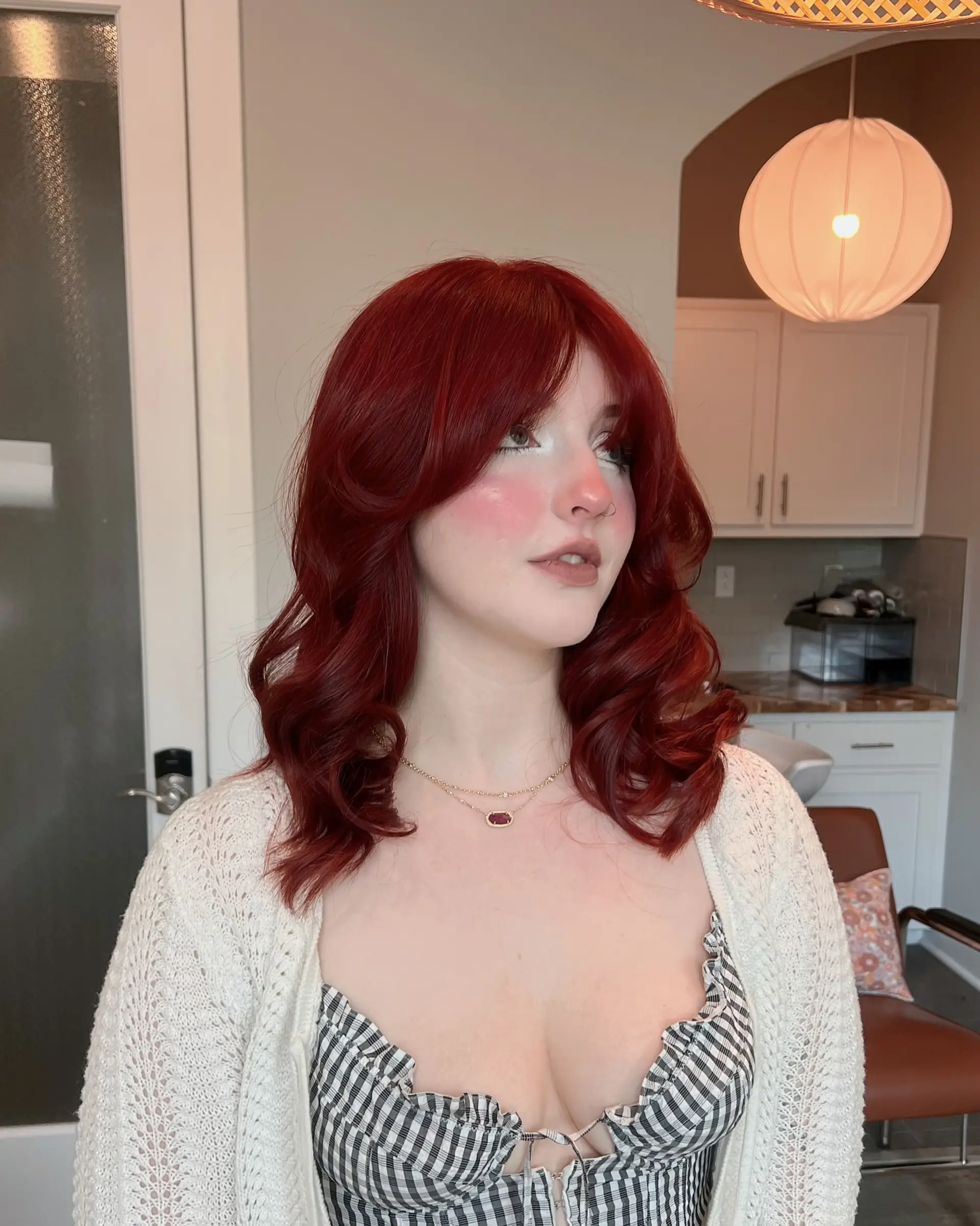 This style features vibrant ruby red, medium-length hair with a modern butterfly cut, incorporating voluminous layers and a full fringe. The hair is styled with soft, bouncy waves for a chic and dynamic finish. 1