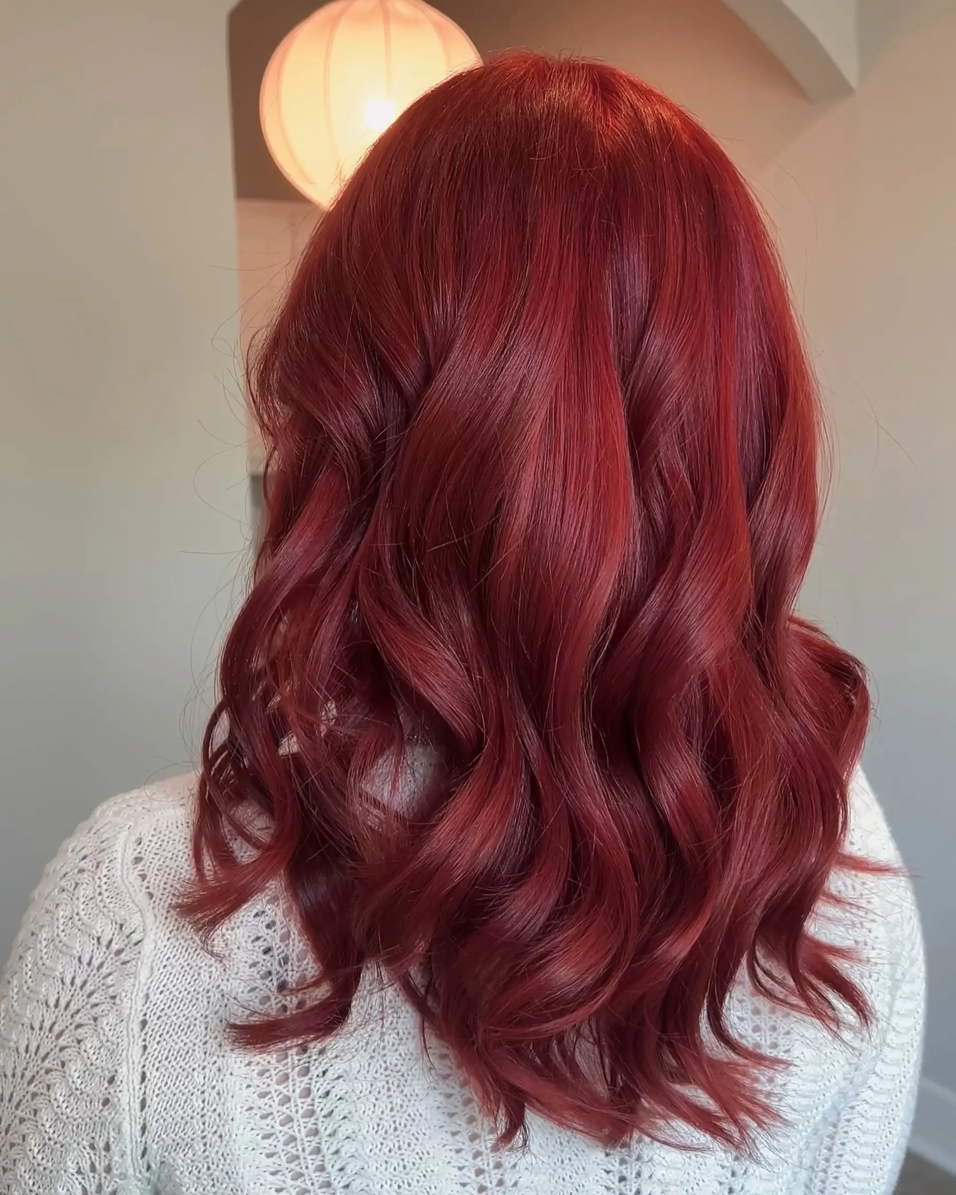 This style features vibrant ruby red, medium-length hair with a modern butterfly cut, incorporating voluminous layers and a full fringe. The hair is styled with soft, bouncy waves for a chic and dynamic finish. 2