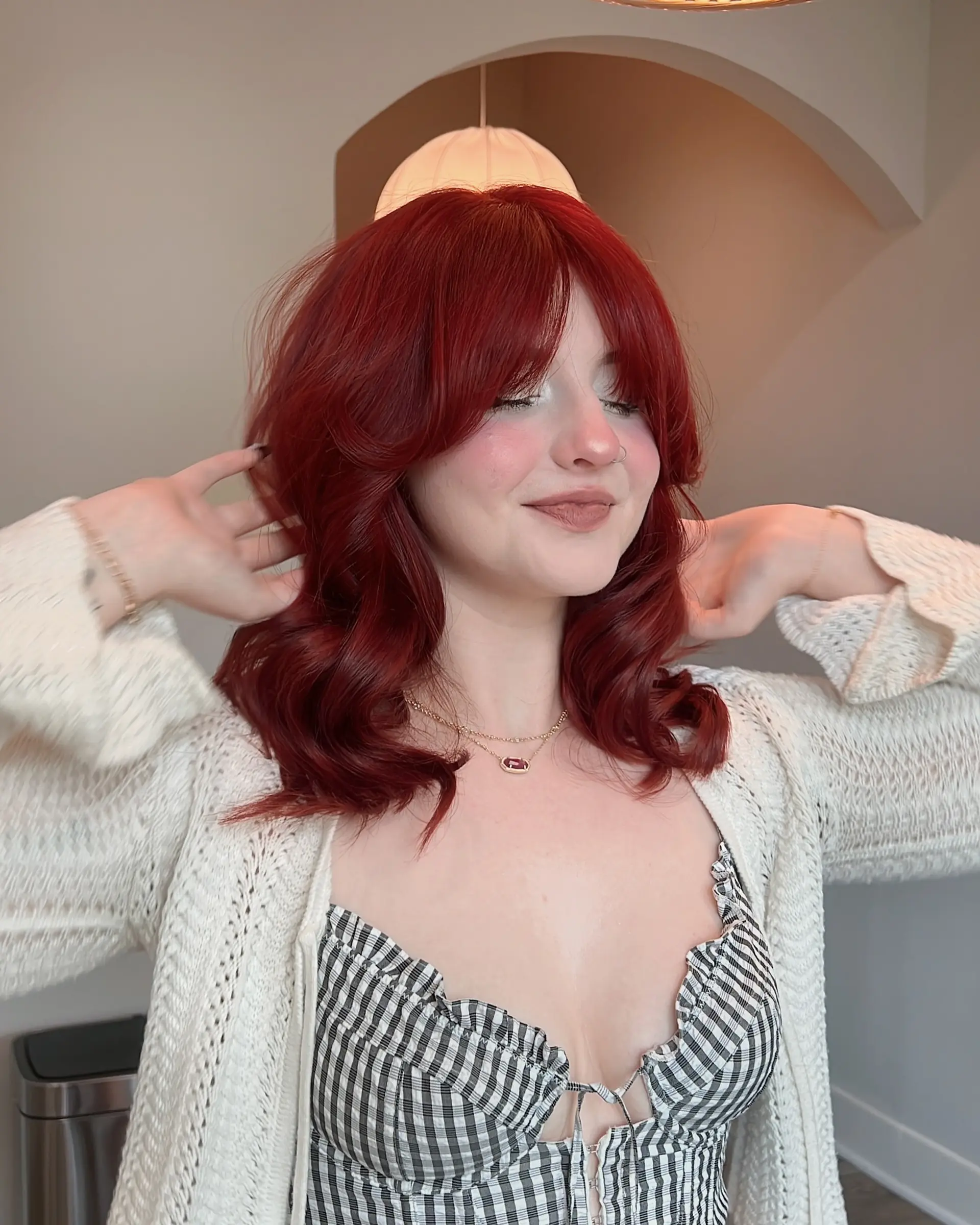 This style features vibrant ruby red, medium-length hair with a modern butterfly cut, incorporating voluminous layers and a full fringe. The hair is styled with soft, bouncy waves for a chic and dynamic finish. 3