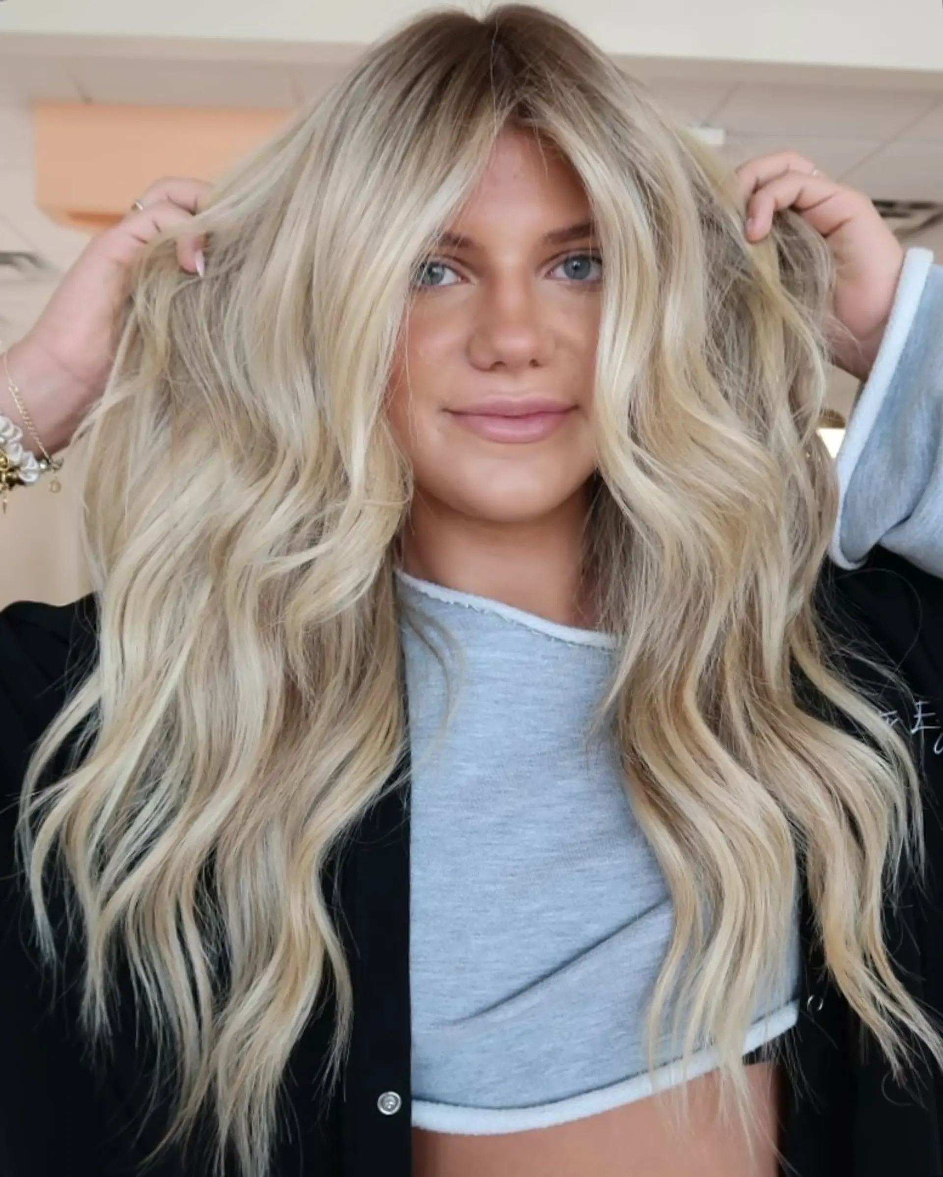 Long lived-in blonde hair featuring a subtle shadow root, blended highlights, and loose, tousled waves with curtain bangs framing the face. 1