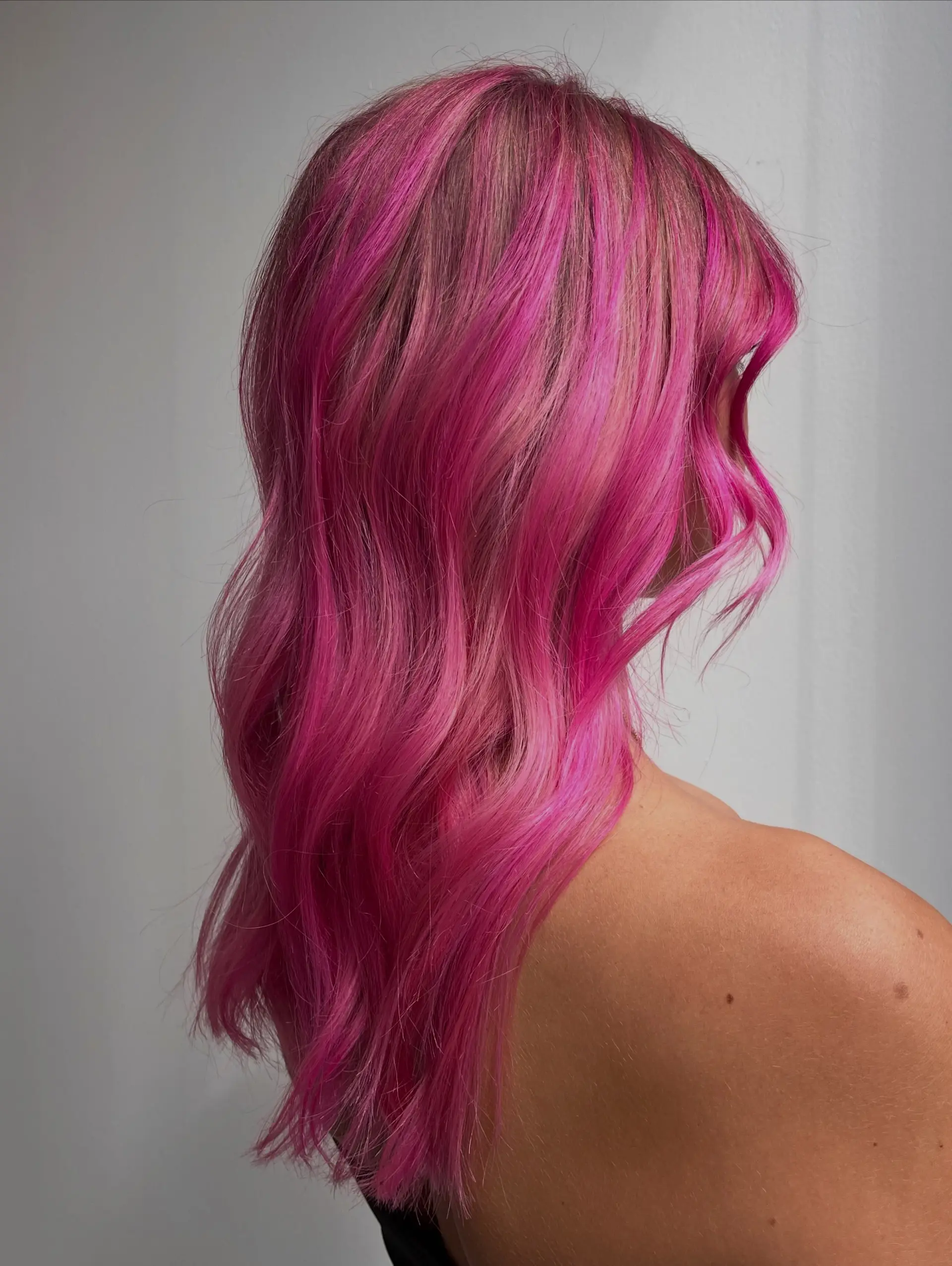 Vibrant magenta and bright pink dimensional hair styled into soft, tousled waves with face-framing layers. 1