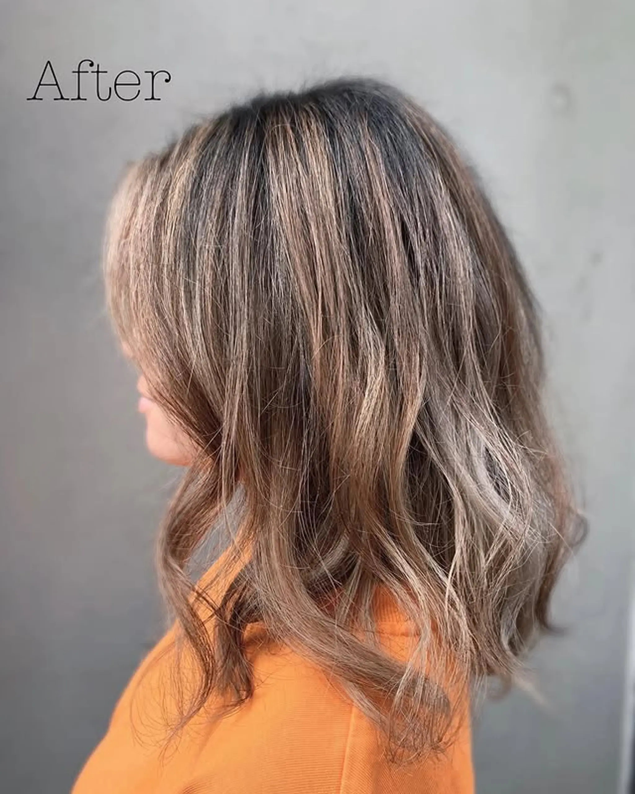A medium-length wavy hairstyle featuring a bronde balayage and trendy curtain bangs.