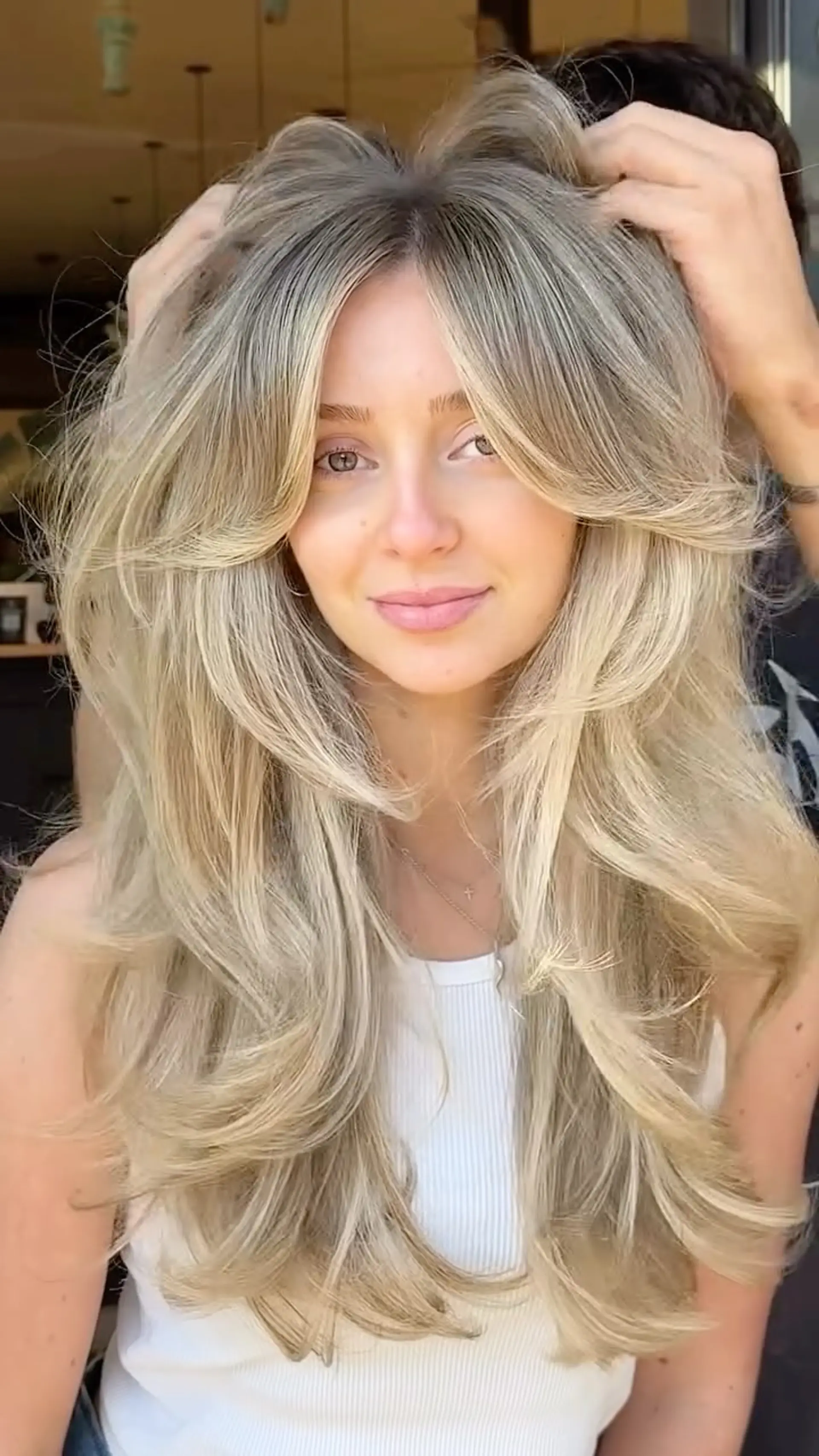 Long, heavily layered butterfly haircut with feathered curtain bangs and a bouncy blowout, featuring dimensional honey blonde highlights. 1