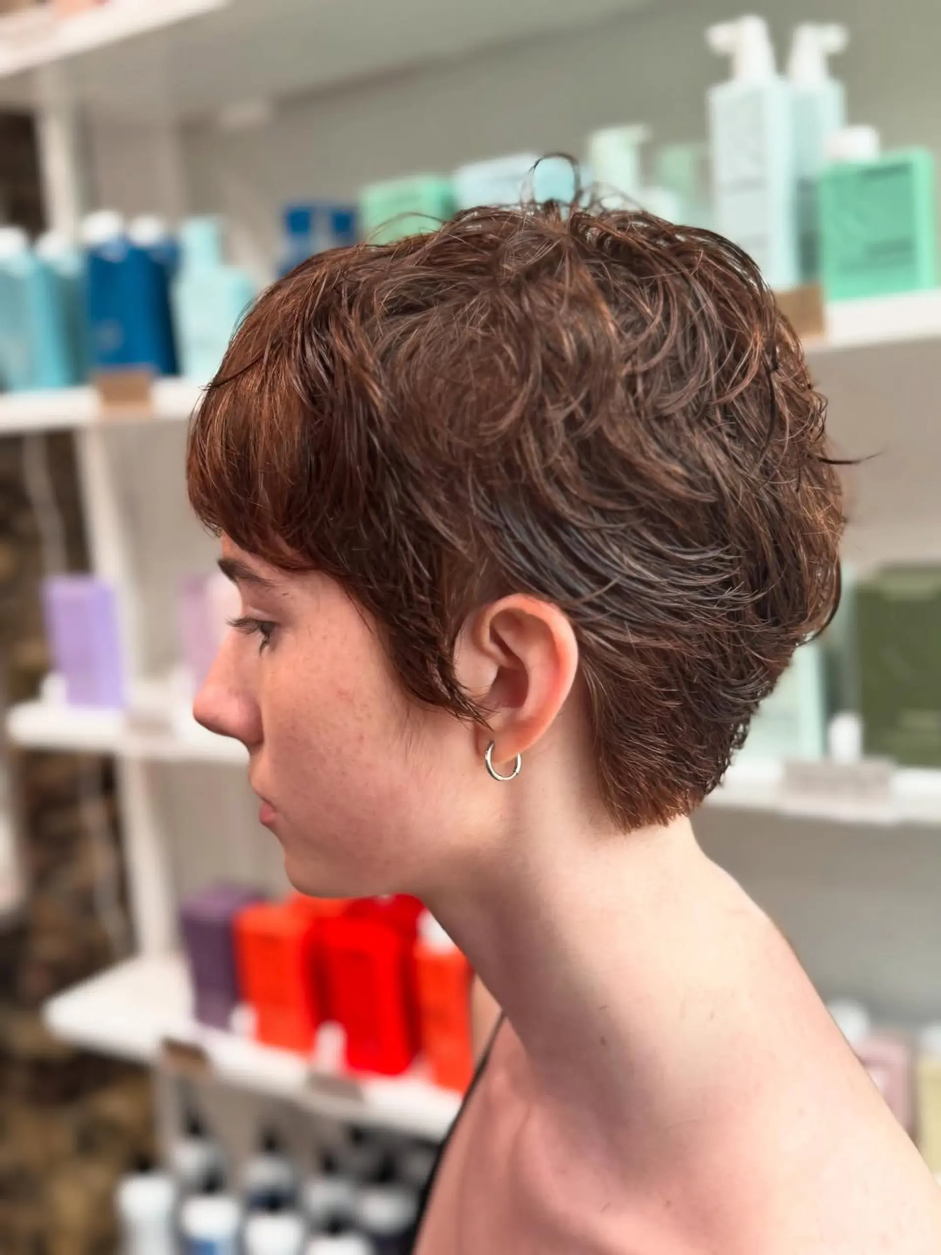 A very short, textured pixie cut with wavy auburn hair, styled shorter on the sides and back for a modern and edgy aesthetic. 1