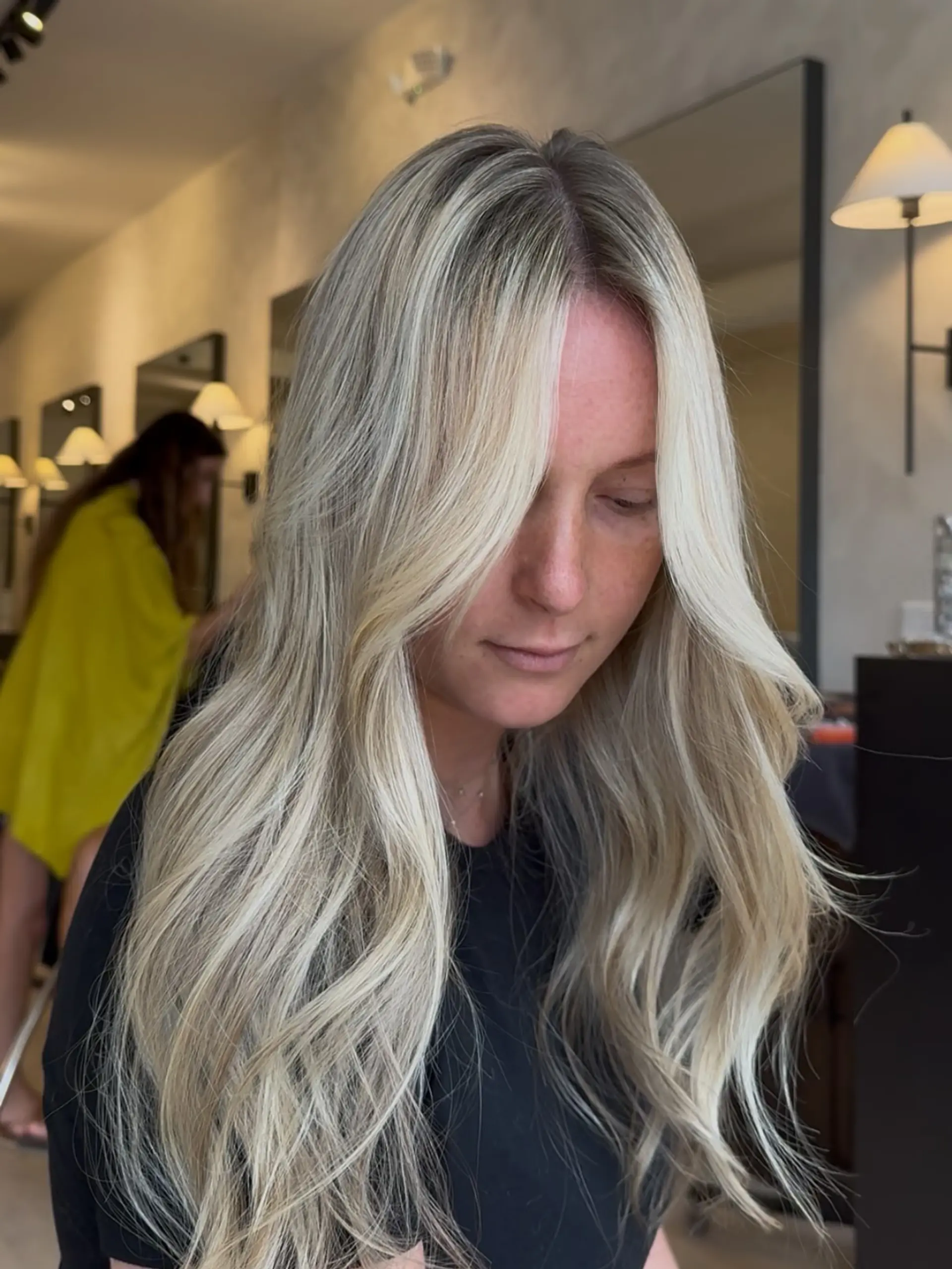 Long cool-toned blonde hair featuring dimensional highlights, a subtle shadow root, and face-framing curtain layers styled in soft waves. 1