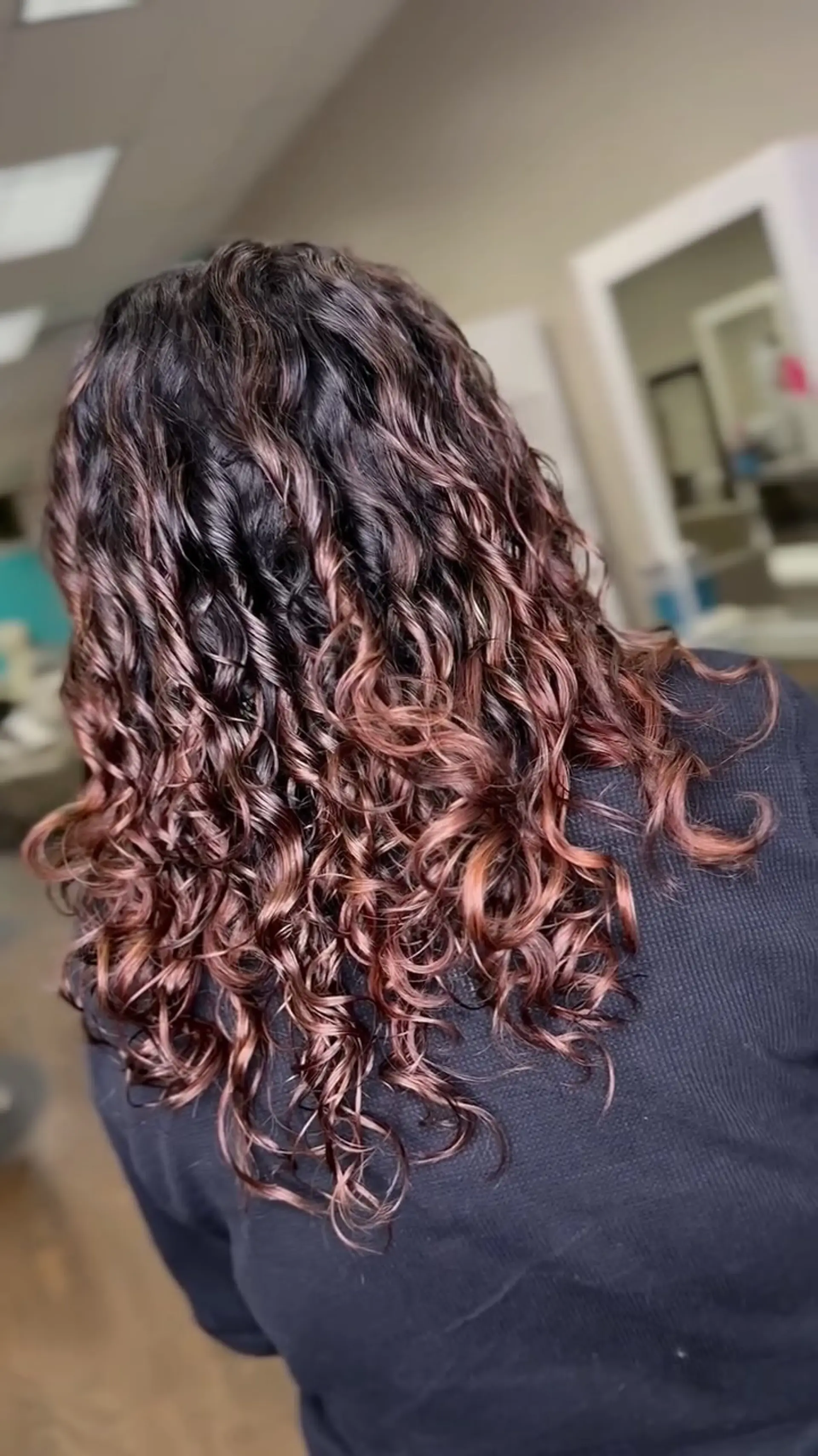 Long defined spiral curls featuring a dark brunette base accented with warm auburn and rose-copper balayage highlights. 1