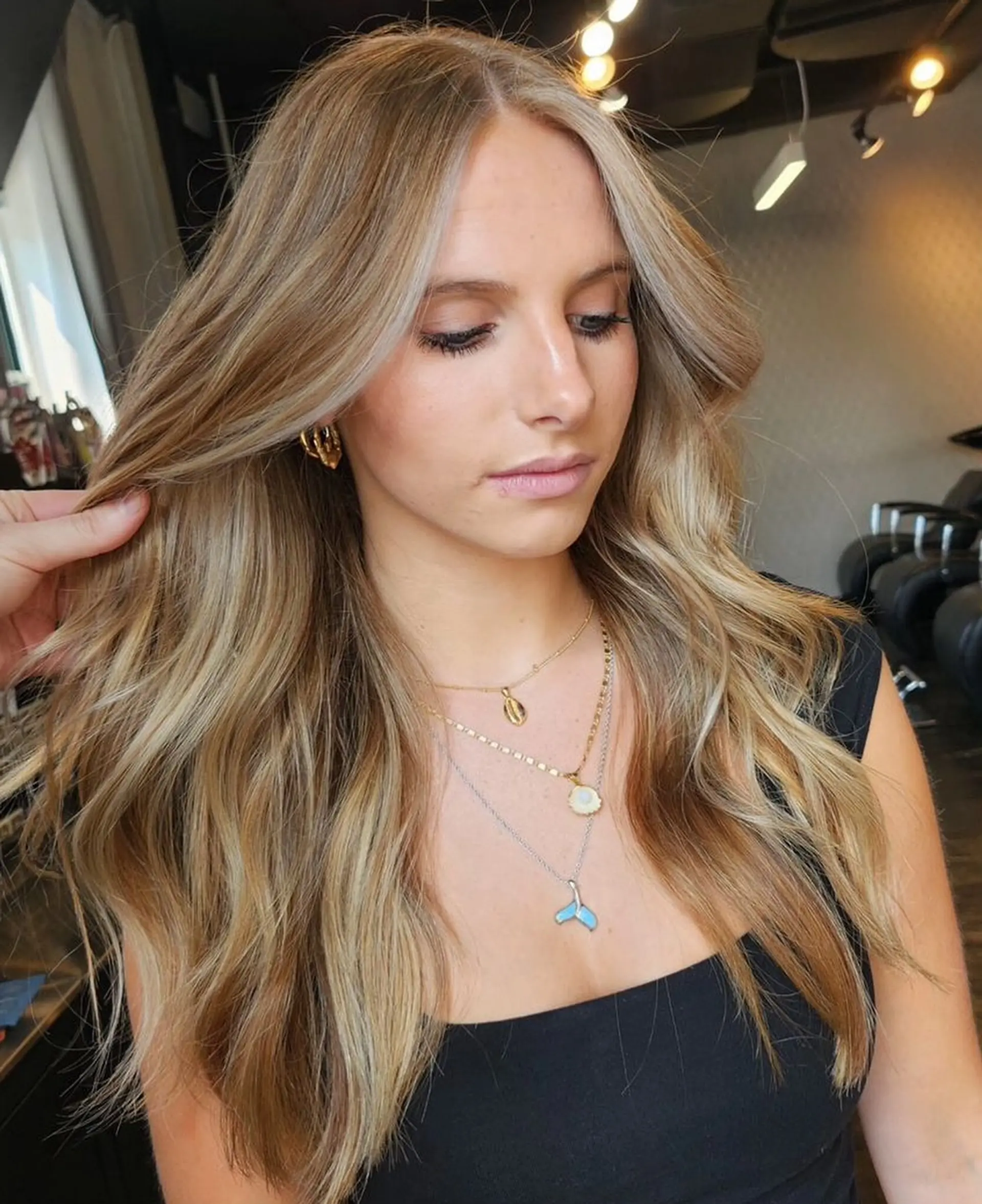Long layered hair styled with soft, loose waves featuring a warm honey blonde balayage and bright face-framing pieces. 1