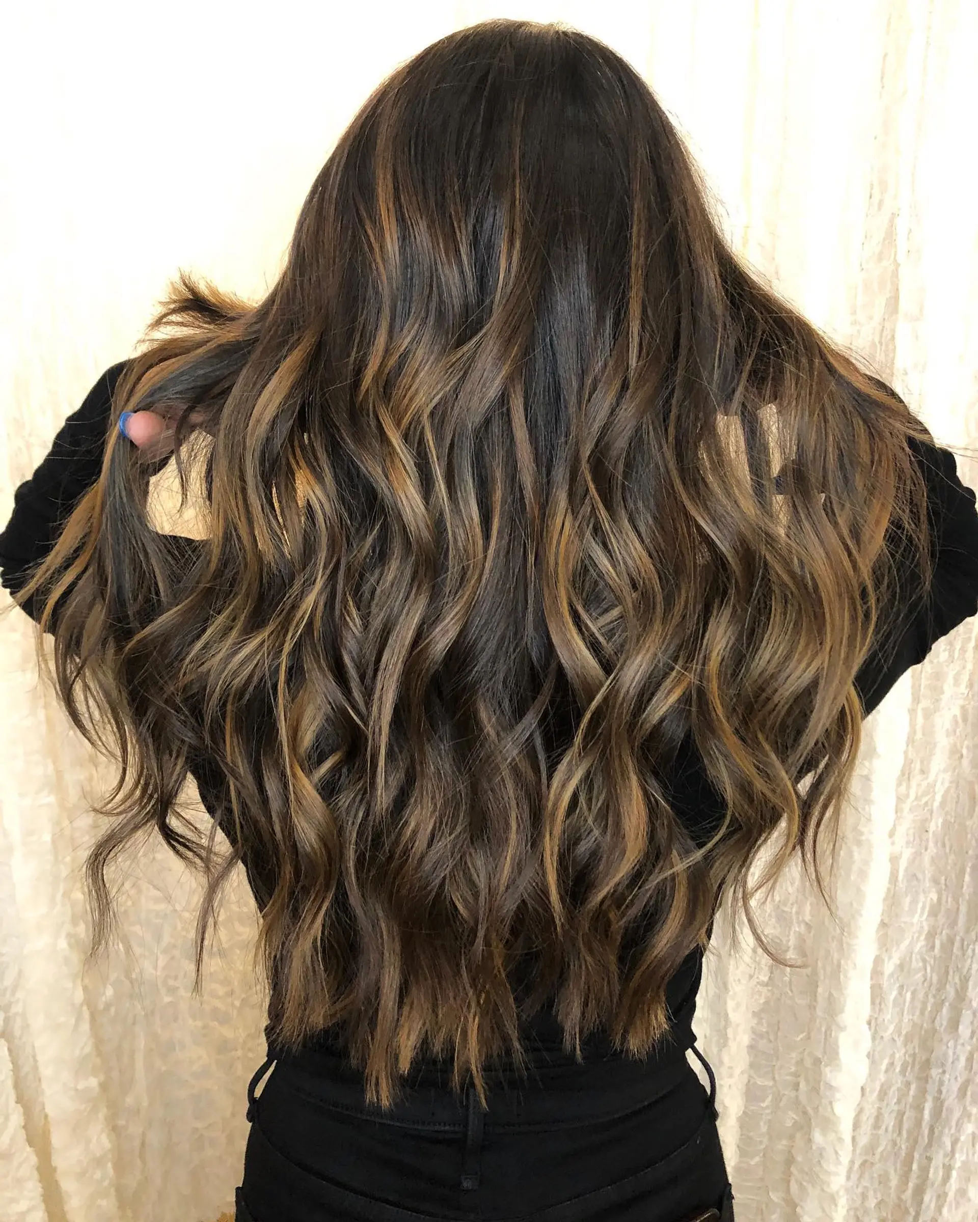Long dark brown hair enhanced with seamless caramel balayage highlights styled in cascading, textured waves. 1