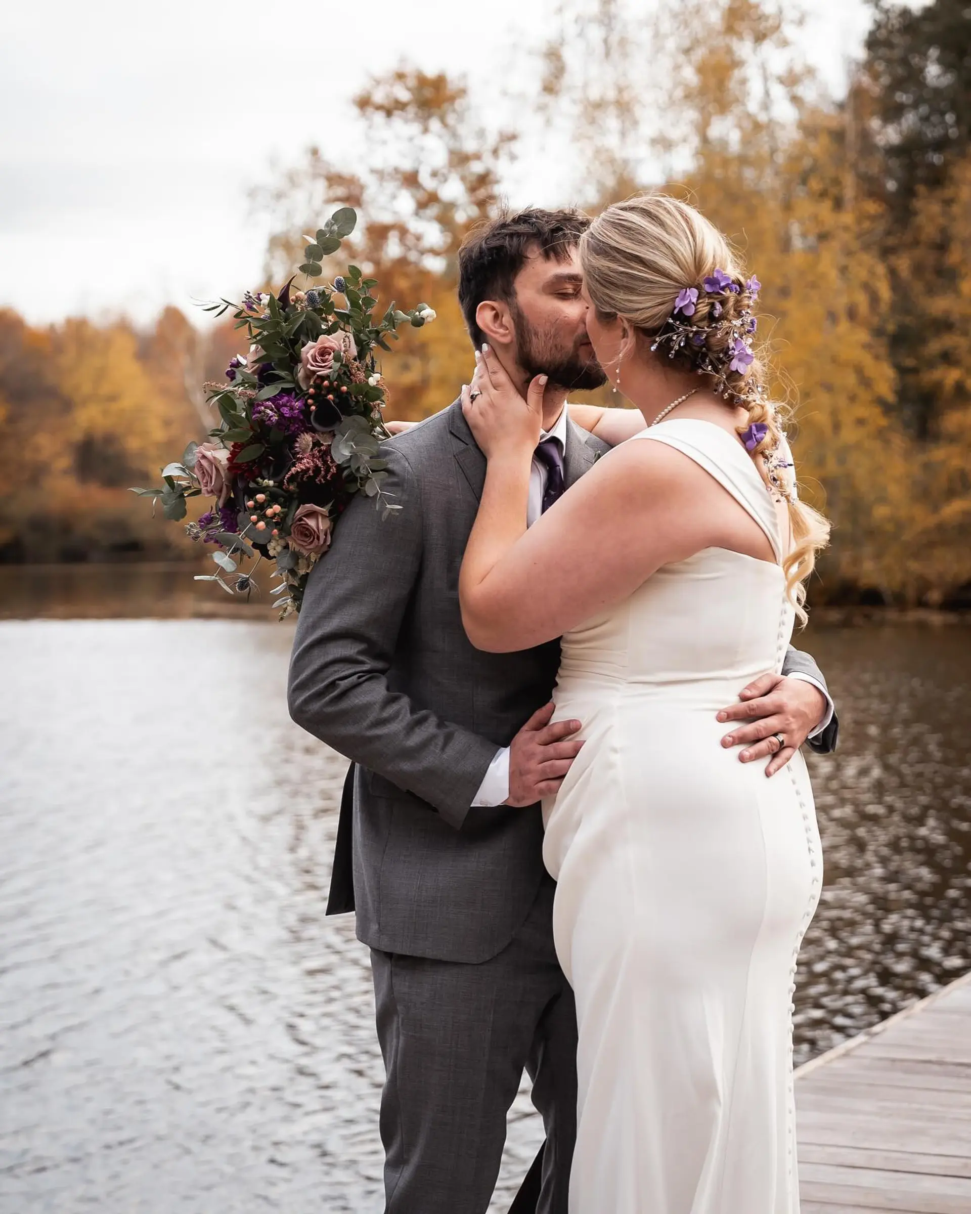 A textured bridal braid elegantly woven with purple floral accessories cascading down the back. 1