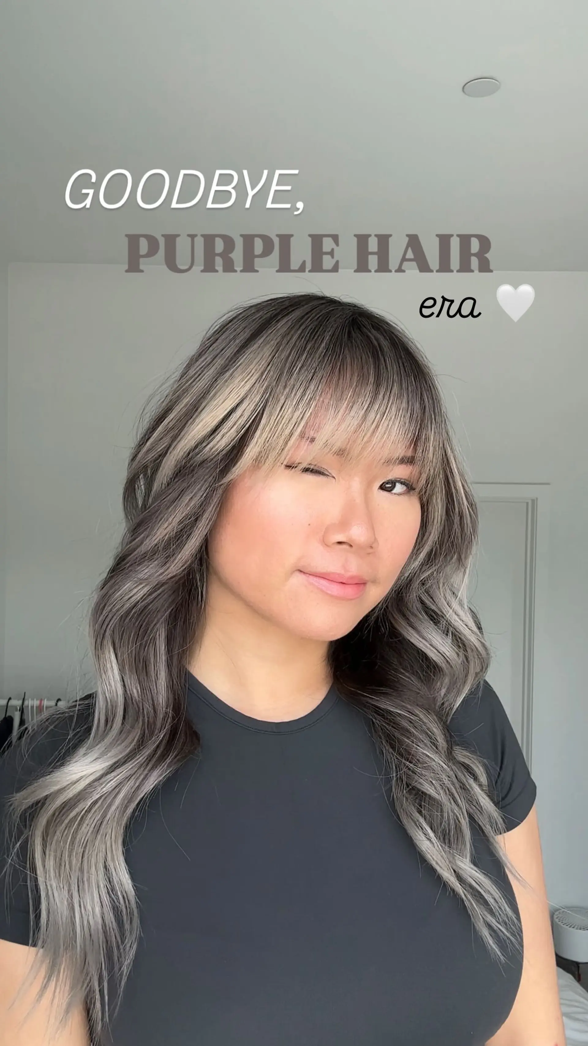 Long cool-toned ash blonde balayage with dark brunette roots, styled in soft waves with light, wispy bangs. 1