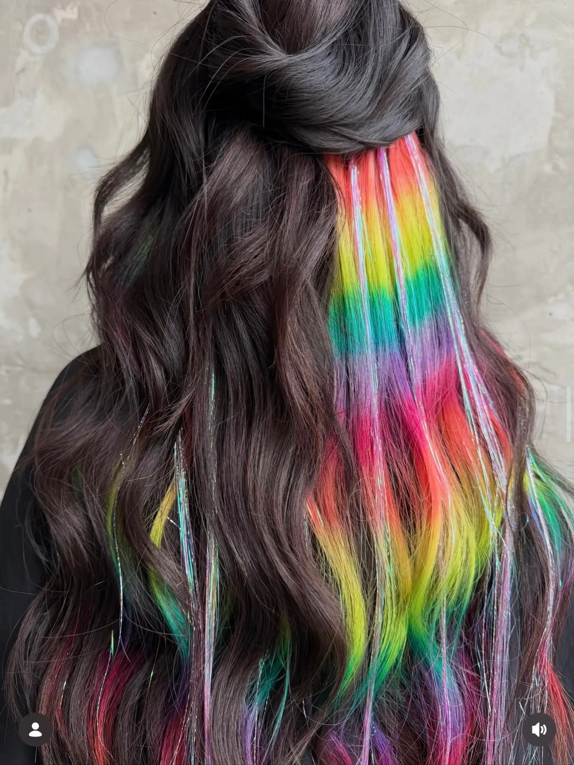 Long, dark wavy hair gathered in a half-up style to reveal vibrant hidden rainbow underlights accented with sparkling hair tinsel. 1