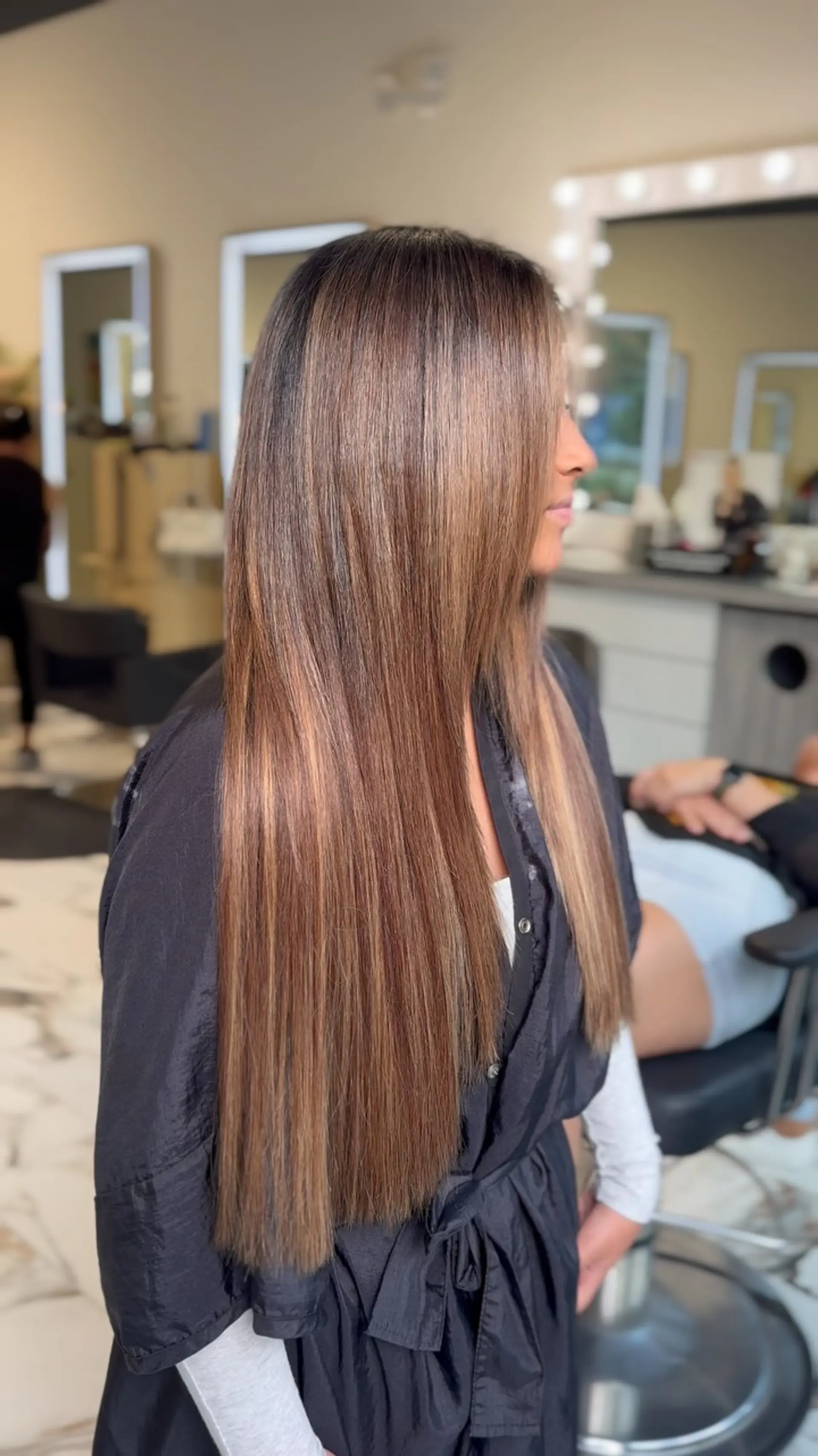 Long, pin-straight brunette hair with seamless multi-tonal warm highlights and blended extensions for added length and thickness. 1