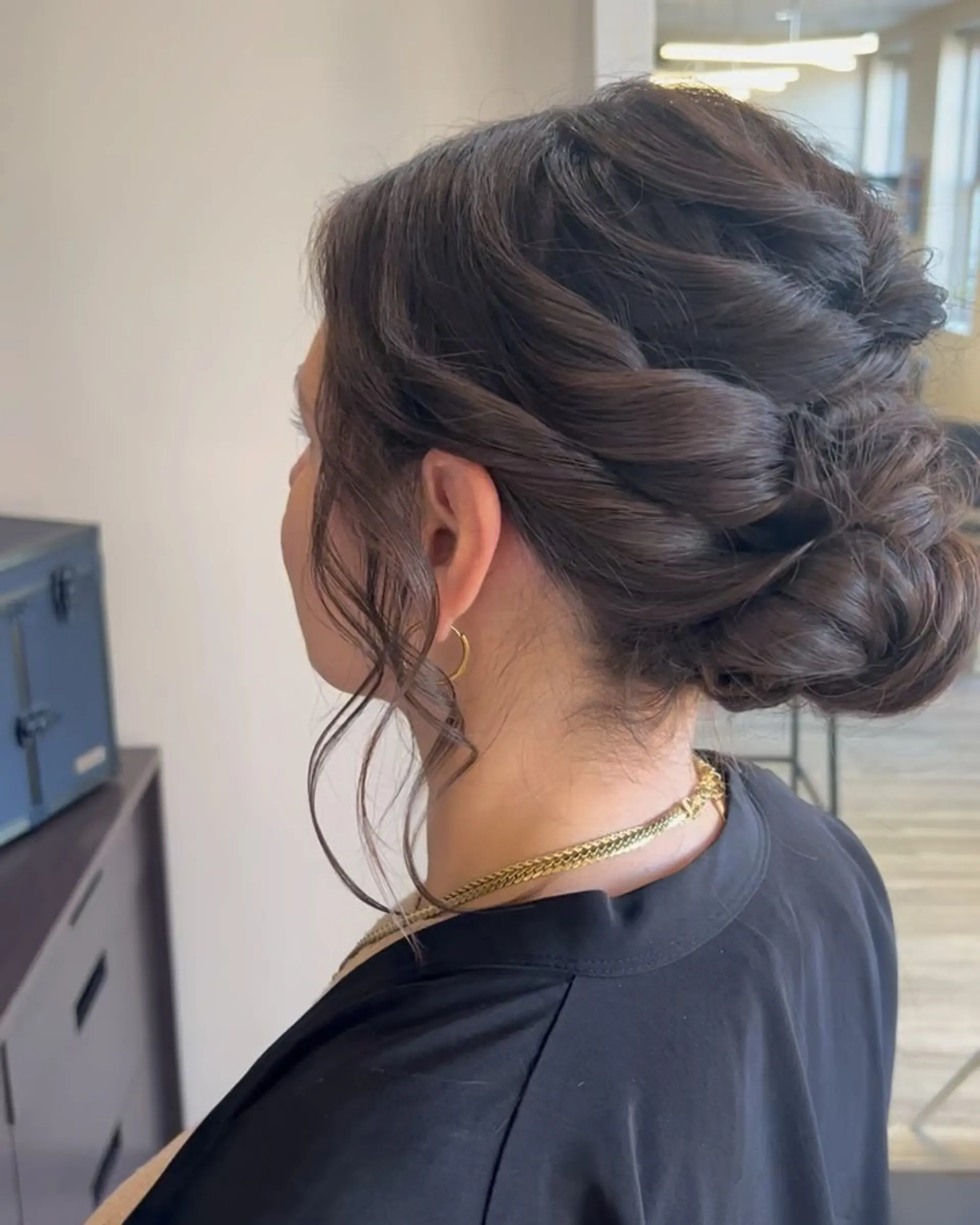 An elegant low updo featuring textured twists woven into a soft bun at the nape with delicate face-framing tendrils. 1