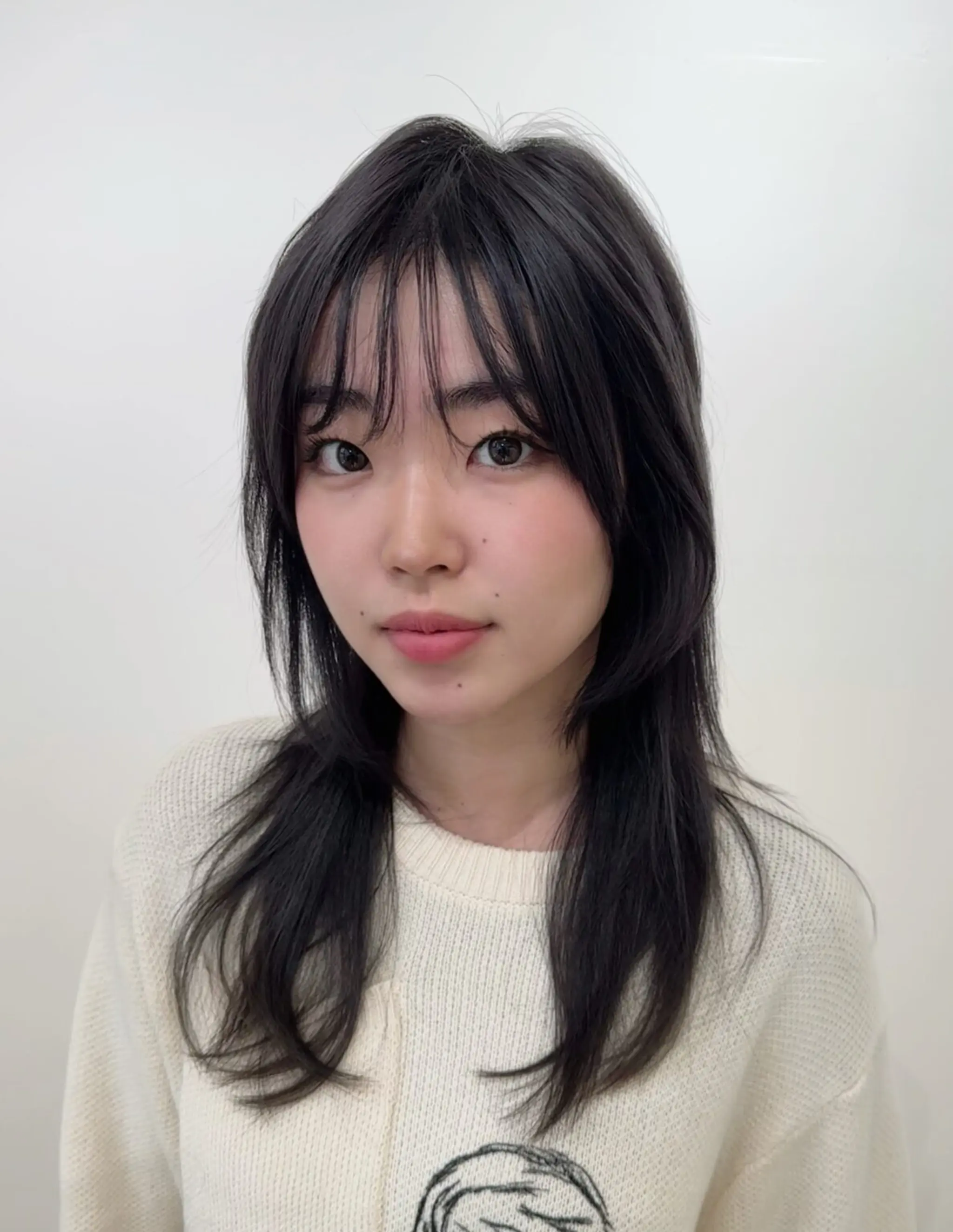 Long, silky black hair with a straight texture, featuring a layered cut with wispy fringe bangs that gently frame the face.