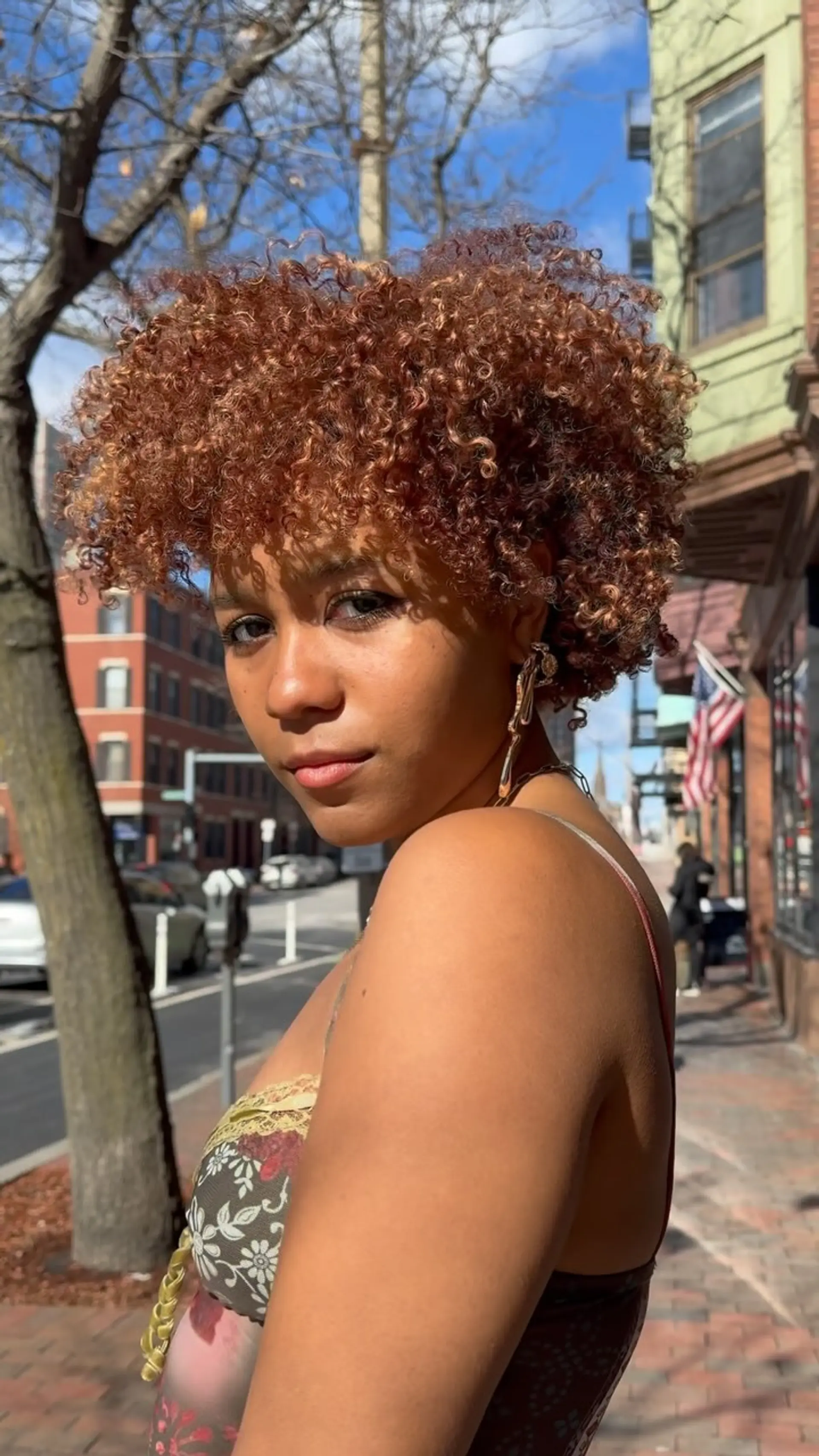 A rounded short cut shaped for tight, defined coils in a warm copper hue with soft curly bangs. 1