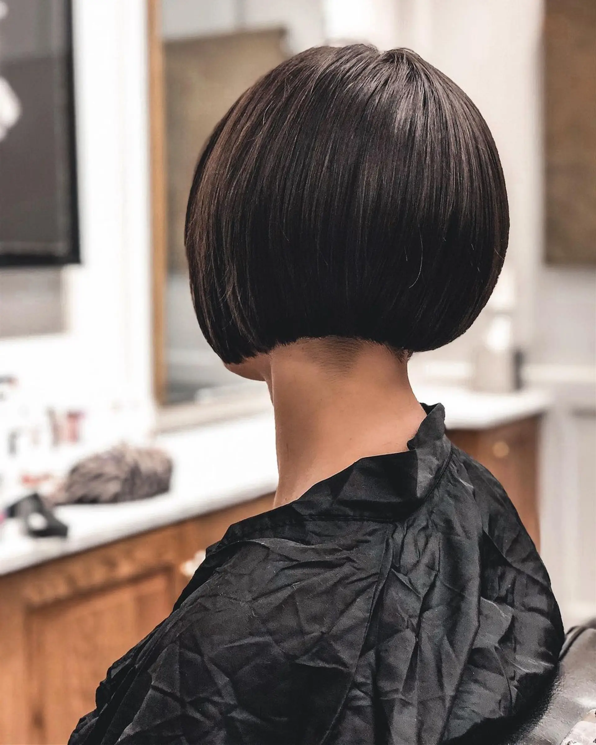 An elegant, short, dark brown bob with a sleek, straight texture. The blunt cut line sits just above the jawline, with a high-shine finish for a chic look. 1