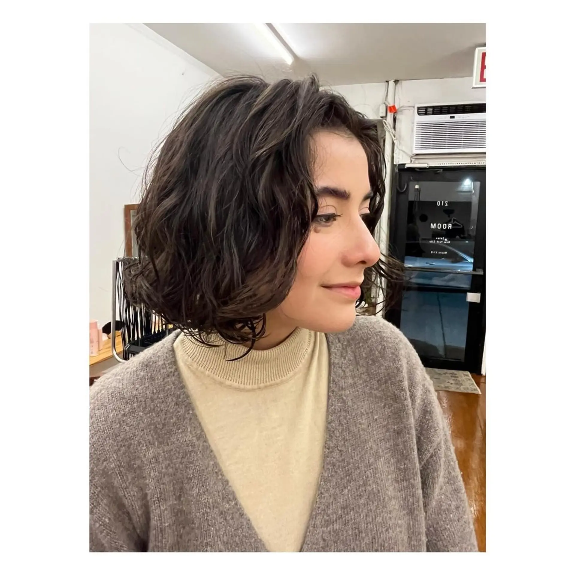 A chic, short bob with a wavy texture and soft curls in dark brown. 1