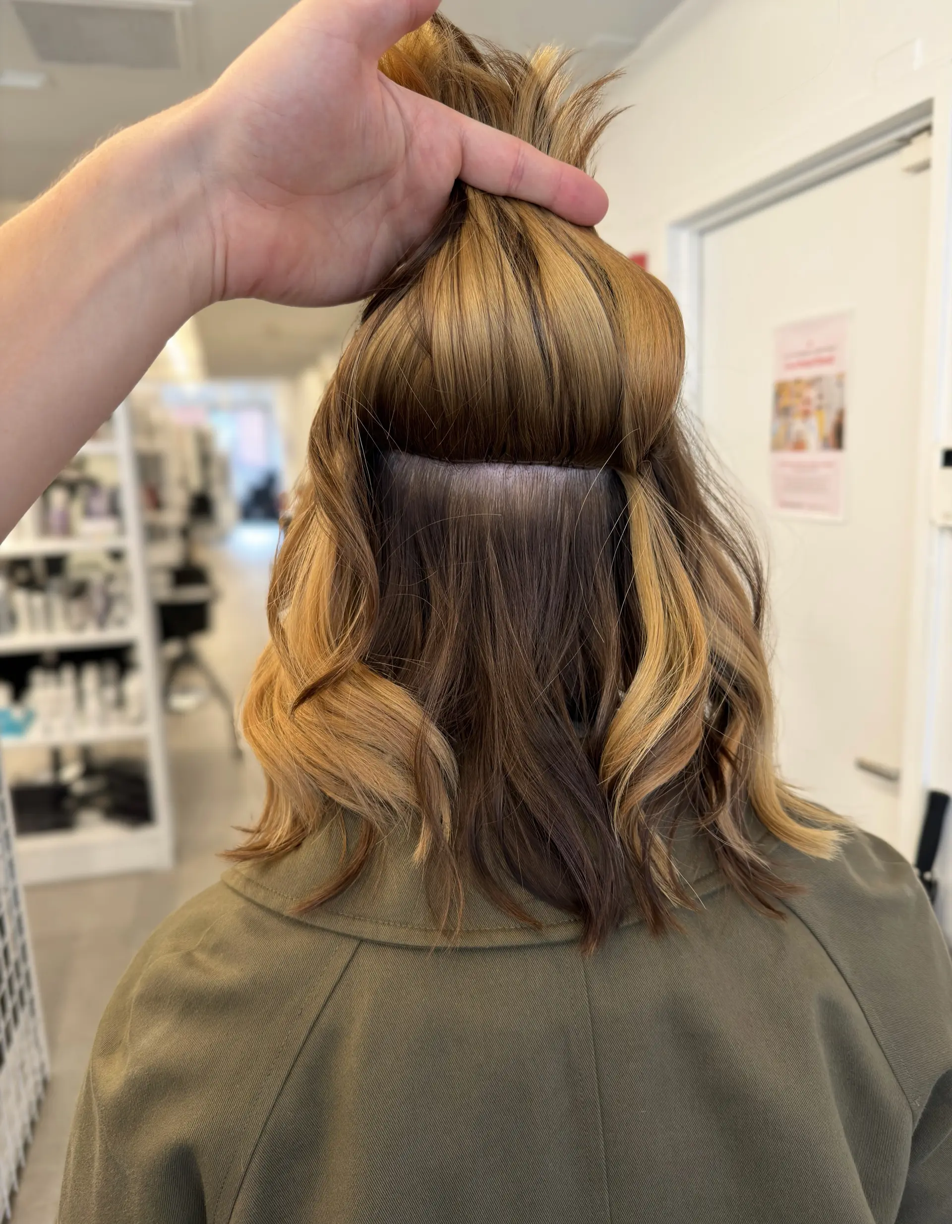 Medium-length wavy hair in golden blonde and brown tones lifted to demonstrate a hand-tied extension track. 1